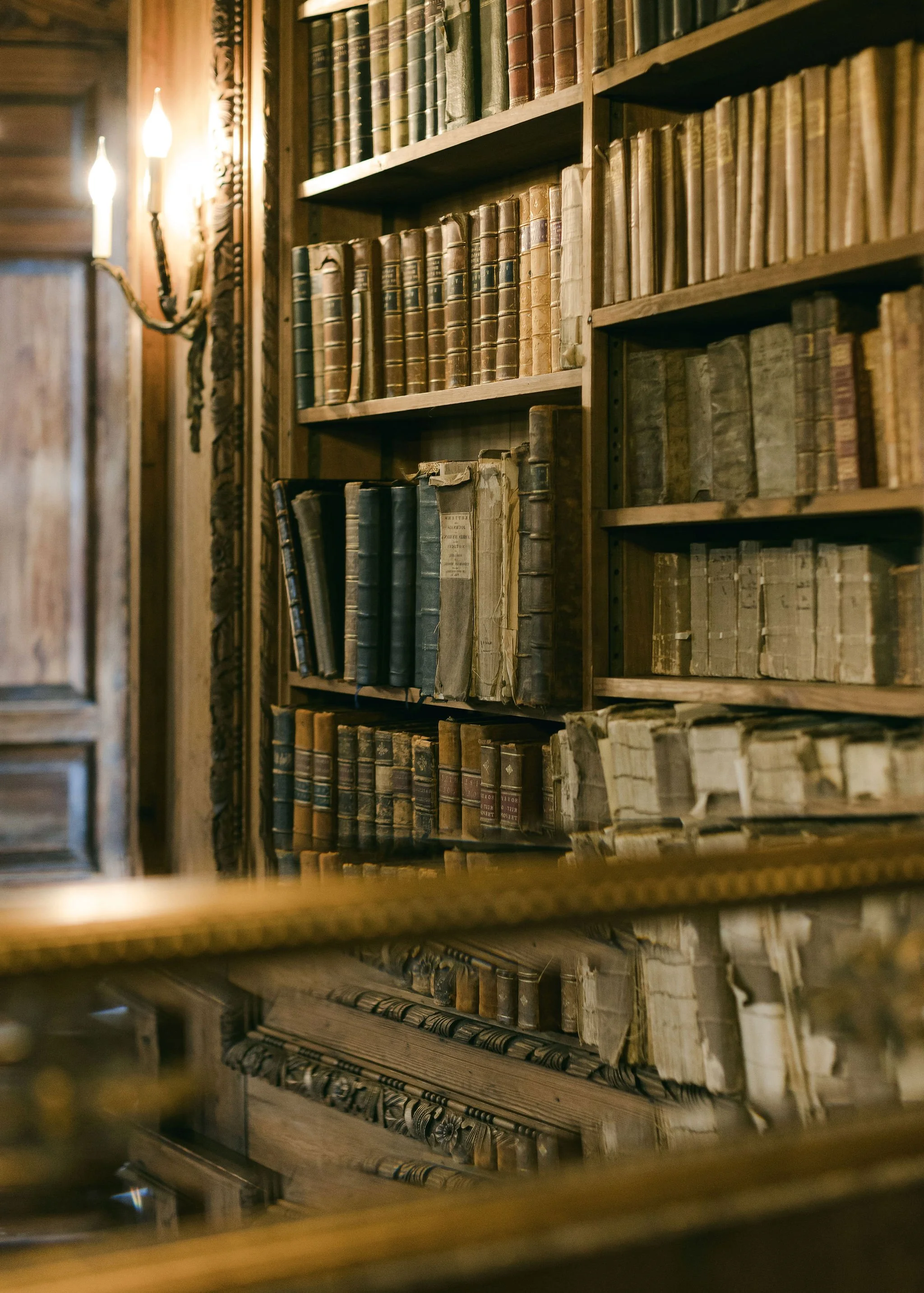 Bookshelves filled with old, worn books in a dimly lit, wooden interior, with a wall-mounted light fixture.