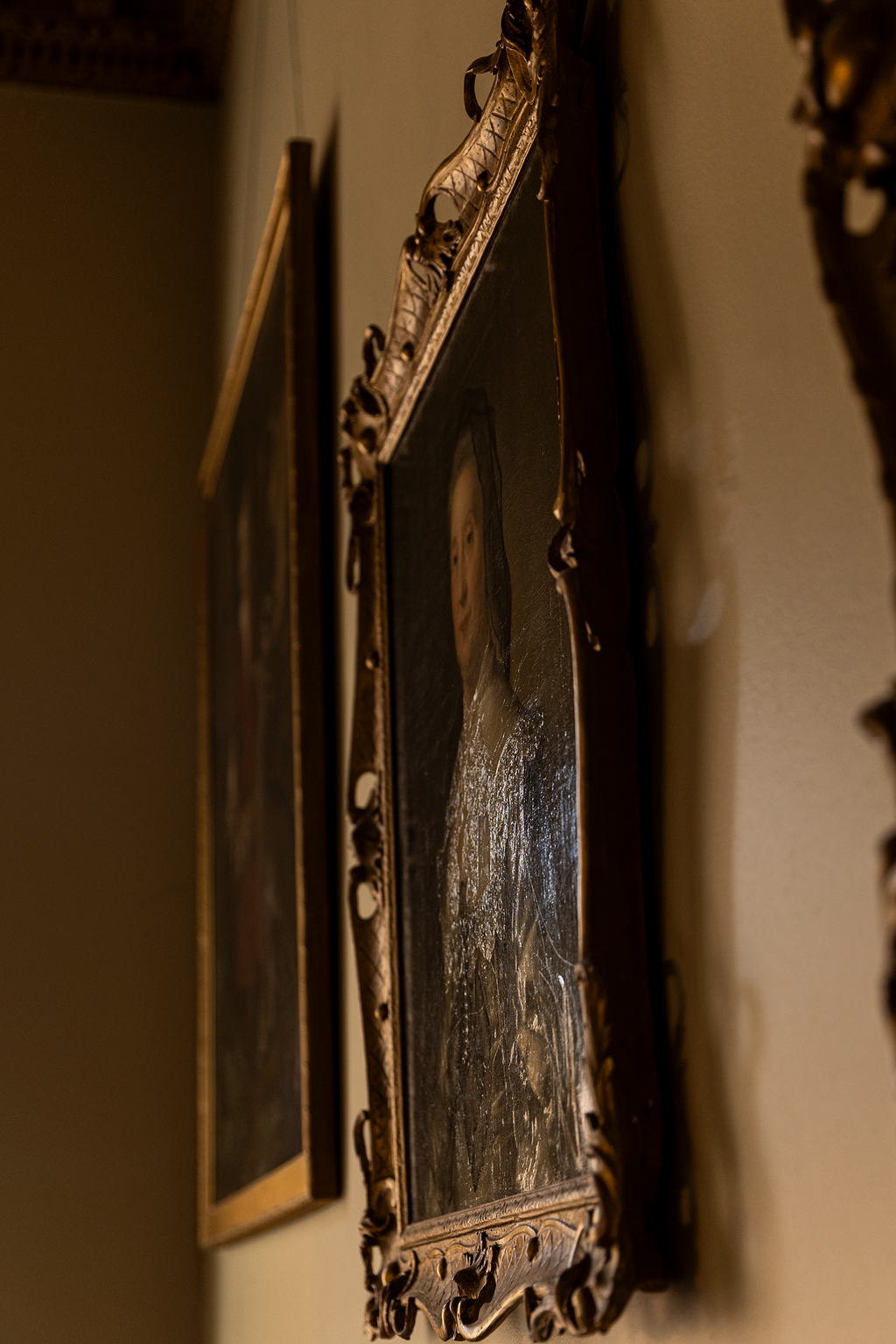 Close-up of an ornate, carved wooden frame surrounding a vintage portrait painting of a woman.