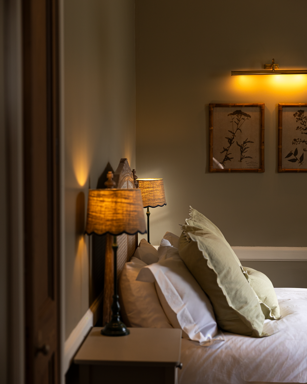 A cozy bedroom with a wooden headboard, beige pillows, and warm lighting from table lamps and wall-mounted lights.