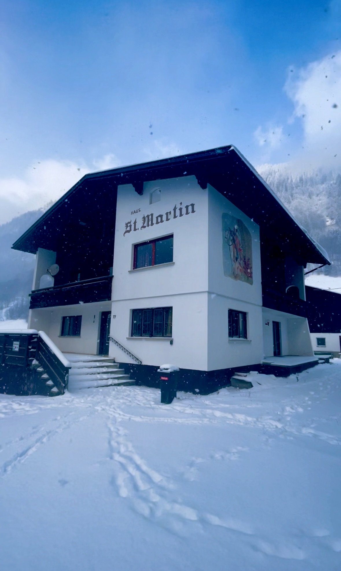 Two-story house in the snow with the inscription "Haus St. Martin", surrounded by snow-covered mountains.
