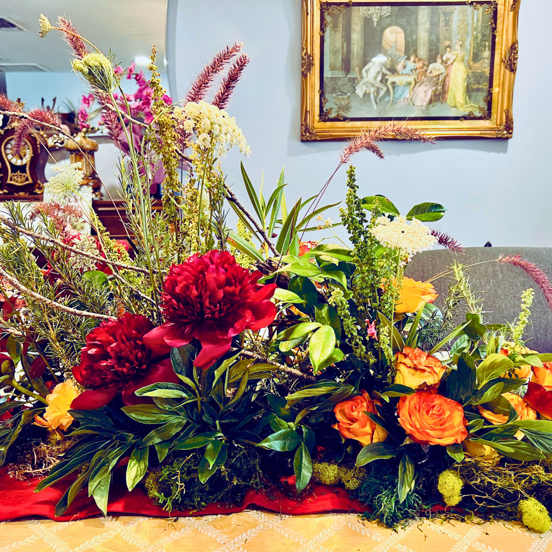 Burgundy peonies, roses, and foraged grasses add to this fall-themed centerpiece