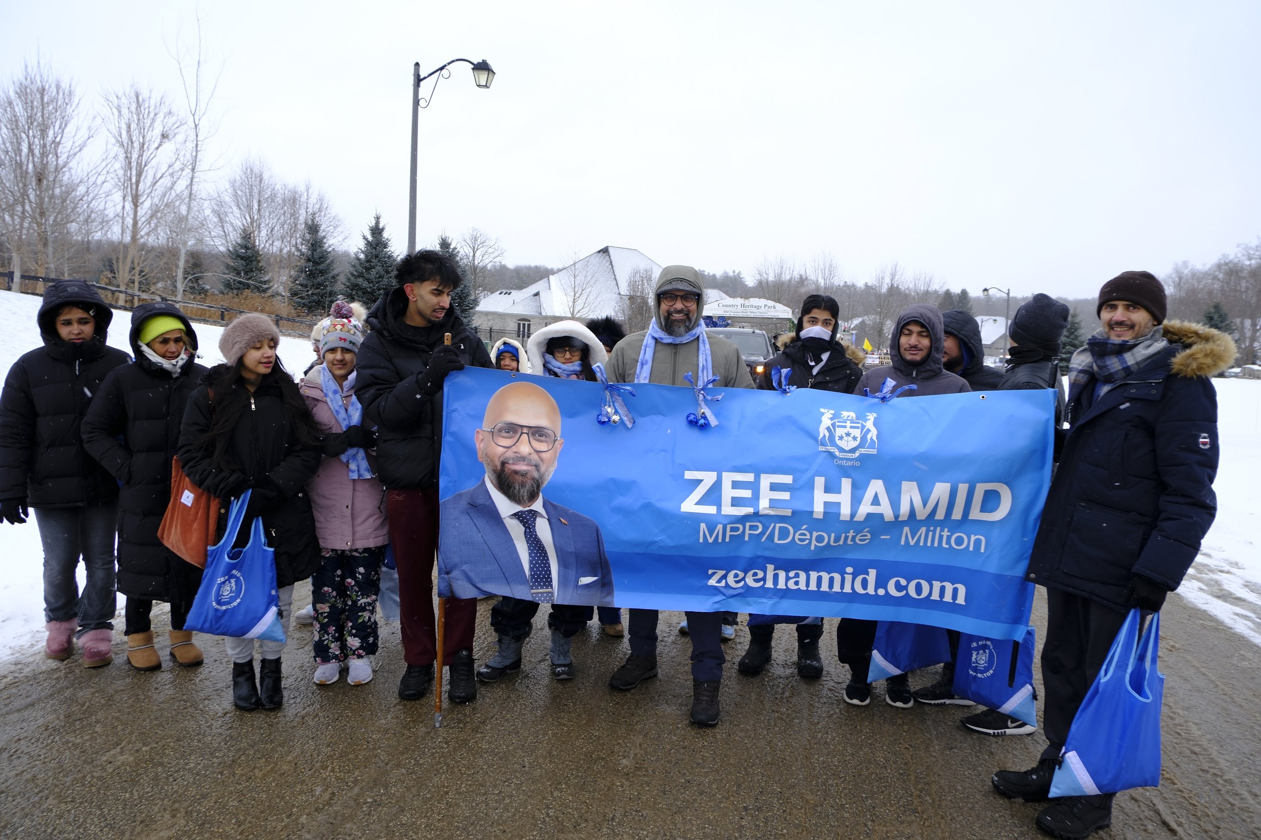 Group of people holding a blue campaign banner for Zee Hamid, standing outdoors in snowy weather.