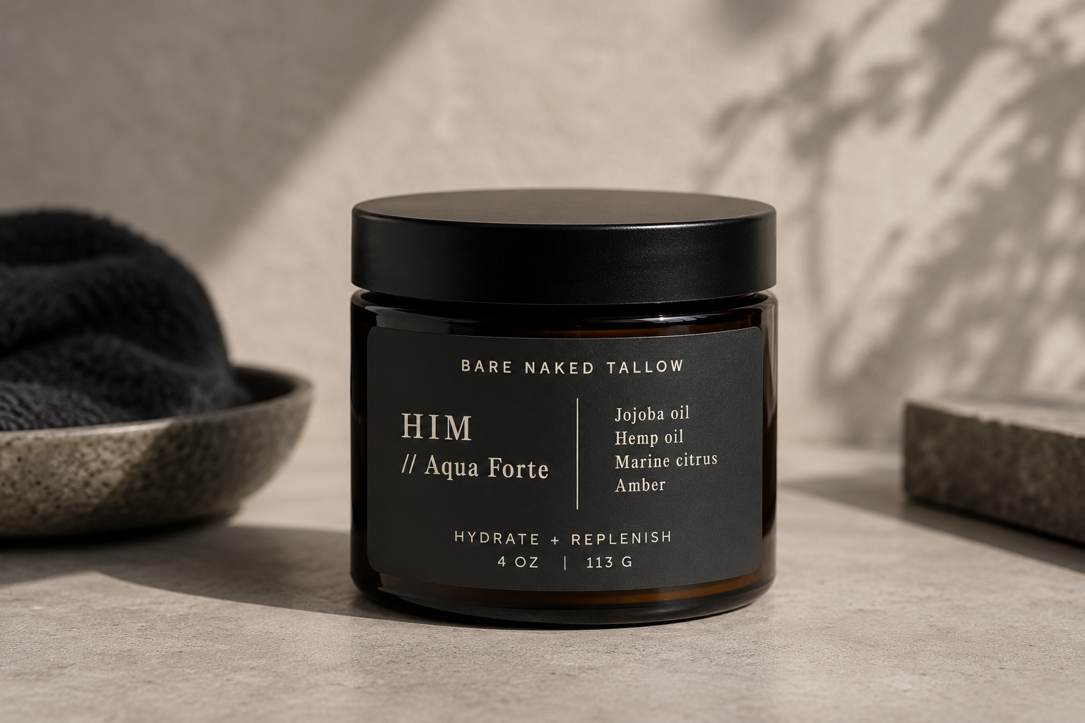 A jar of Bare Naked Tallow Aqua Forte After Shower Cream with Marine Citrus and Amber on a bathroom counter with folded towels and a soap dispenser in the background.