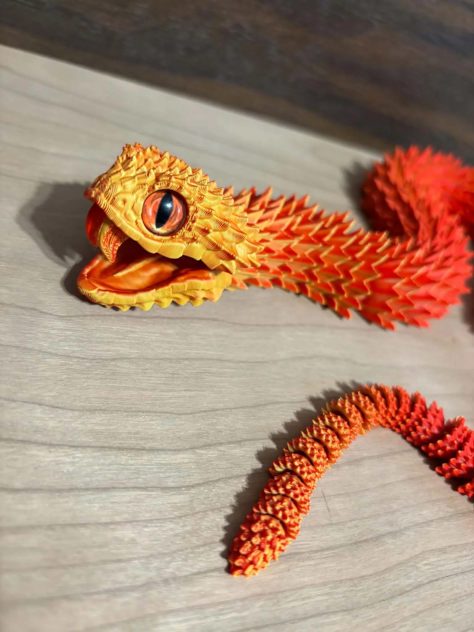 Bright orange and red dragon-shaped decorative object with a large eye and textured spikes on a wooden surface