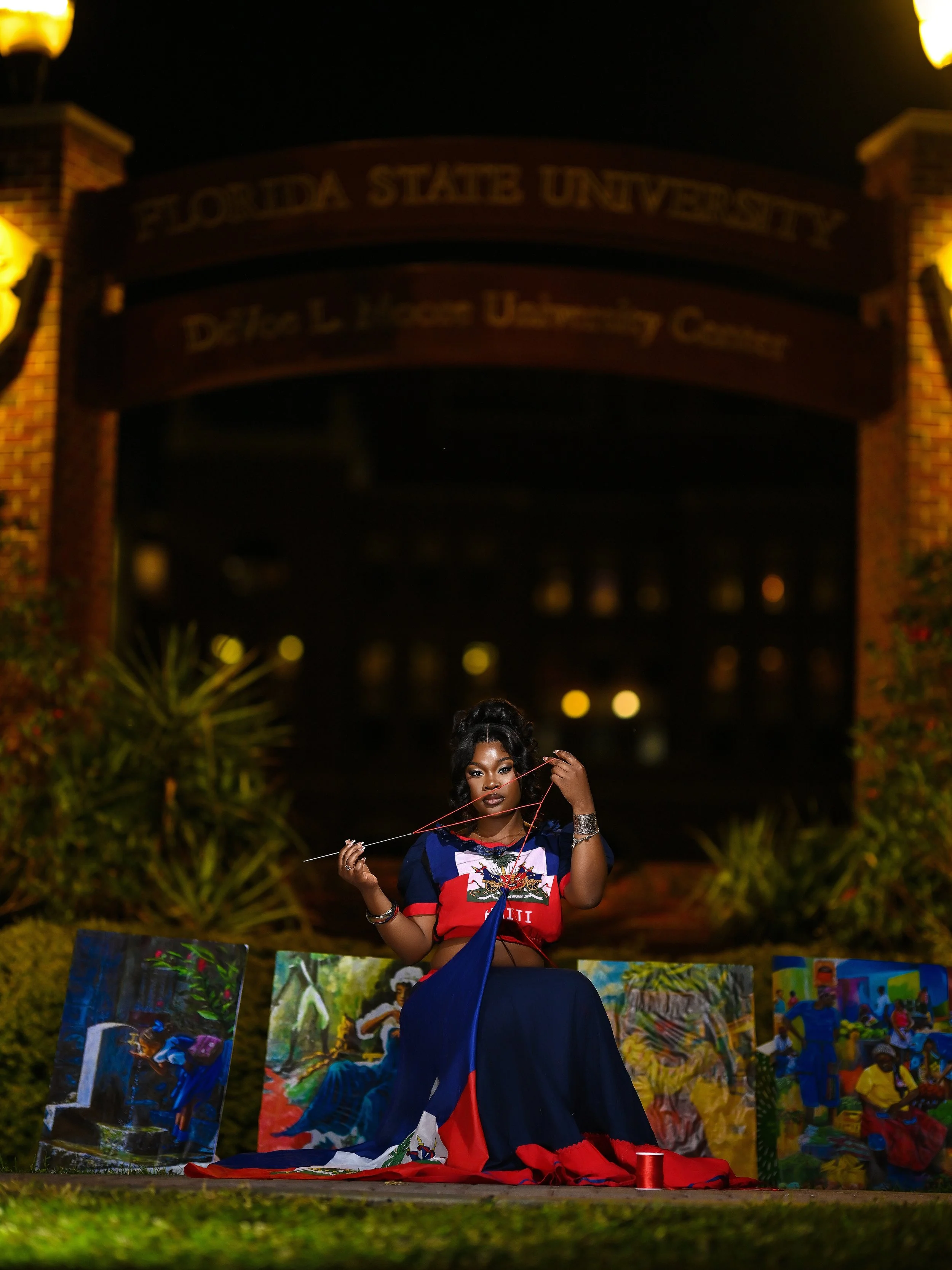 A woman posed in front of colorful paintings outdoors at night, with the University of Florida sign illuminated in the background.