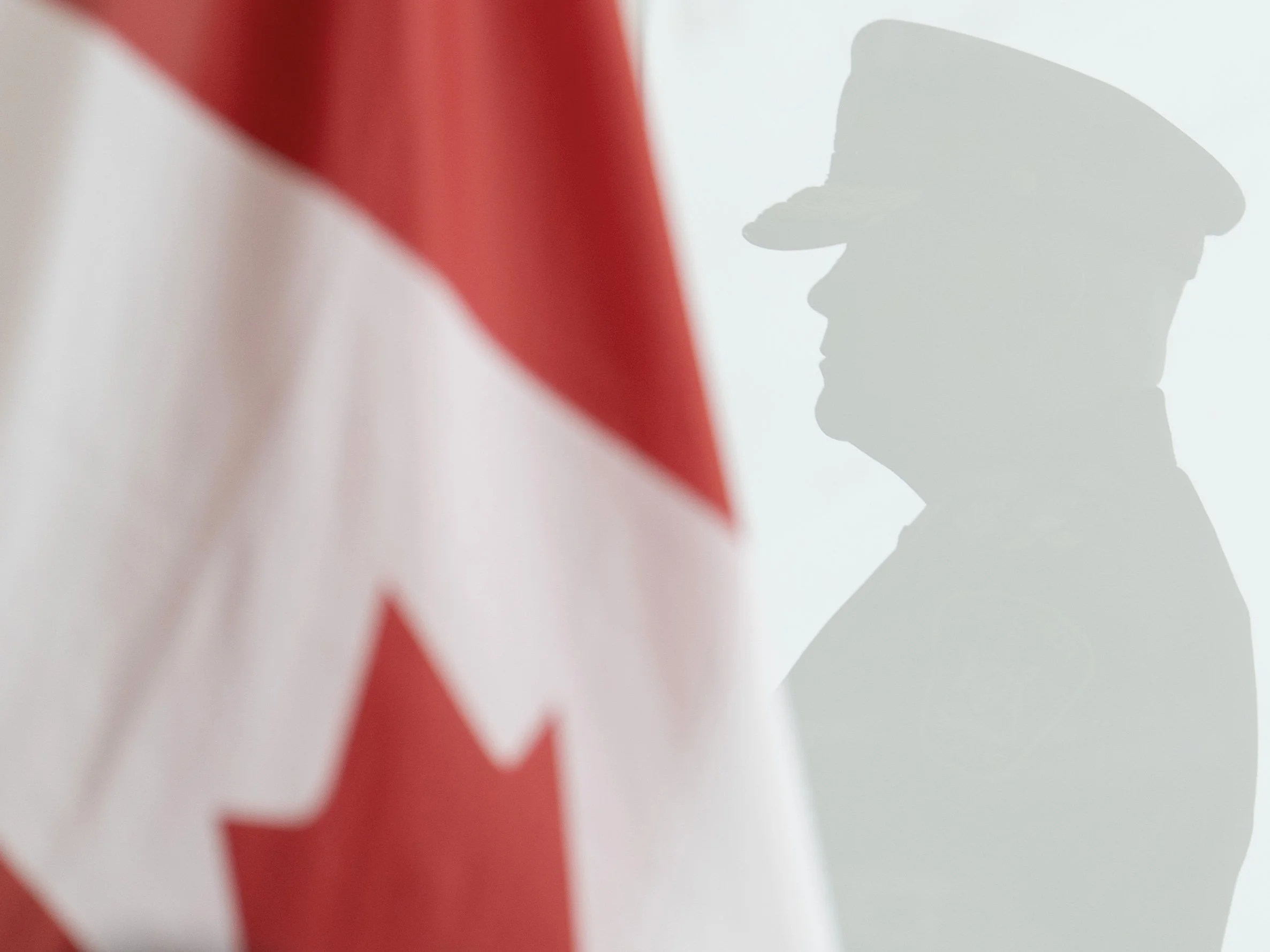 An officer's silhouette is reflected in a glass pane behind the Canadian flag during a press conference at the Belleville Police Service headquarters in Belleville, Ont., on Thursday, Sept. 24, 2026, following updates on the synagogue shooting invest