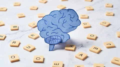Paper cutout of a brain placed among scattered letter tiles on a white background.