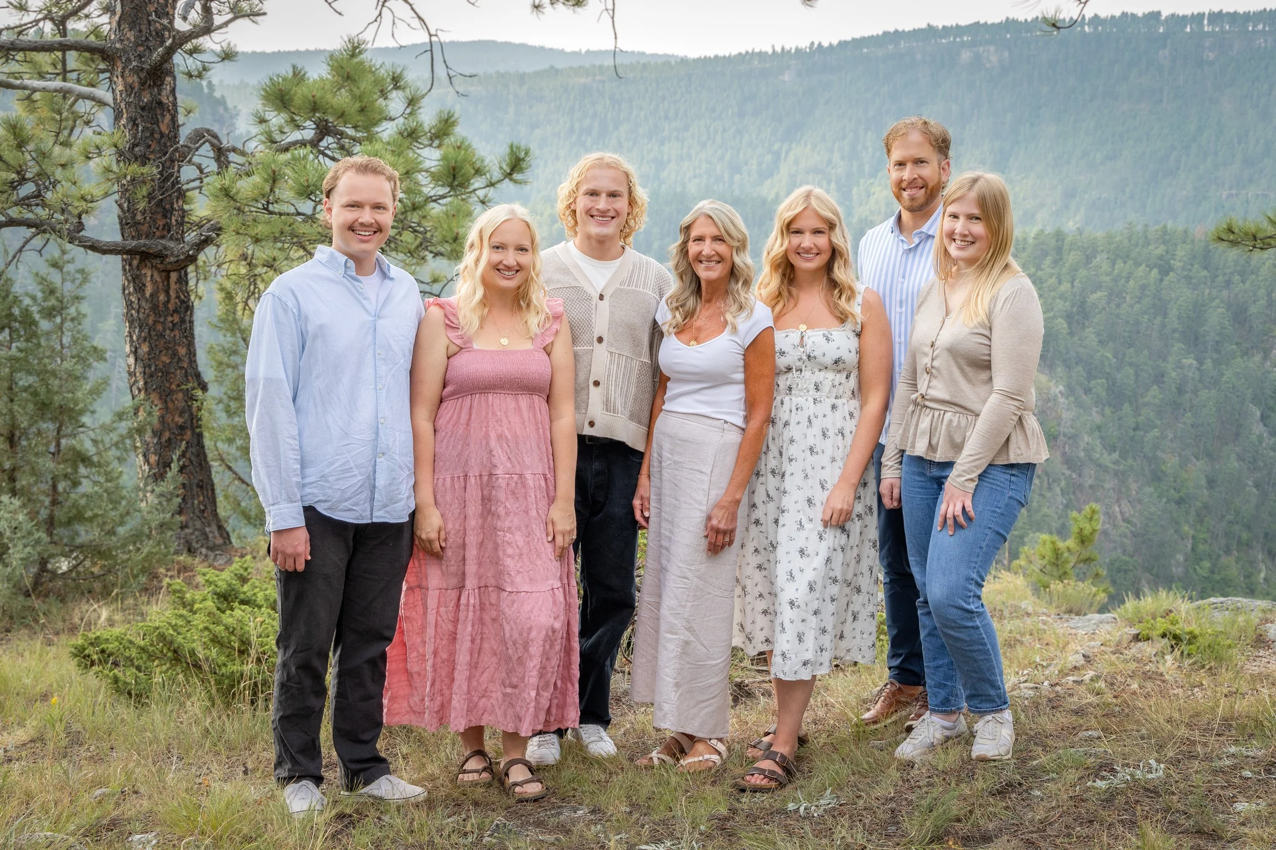 Group of seven people standing outdoors in a forested mountain area, smiling for the camera.