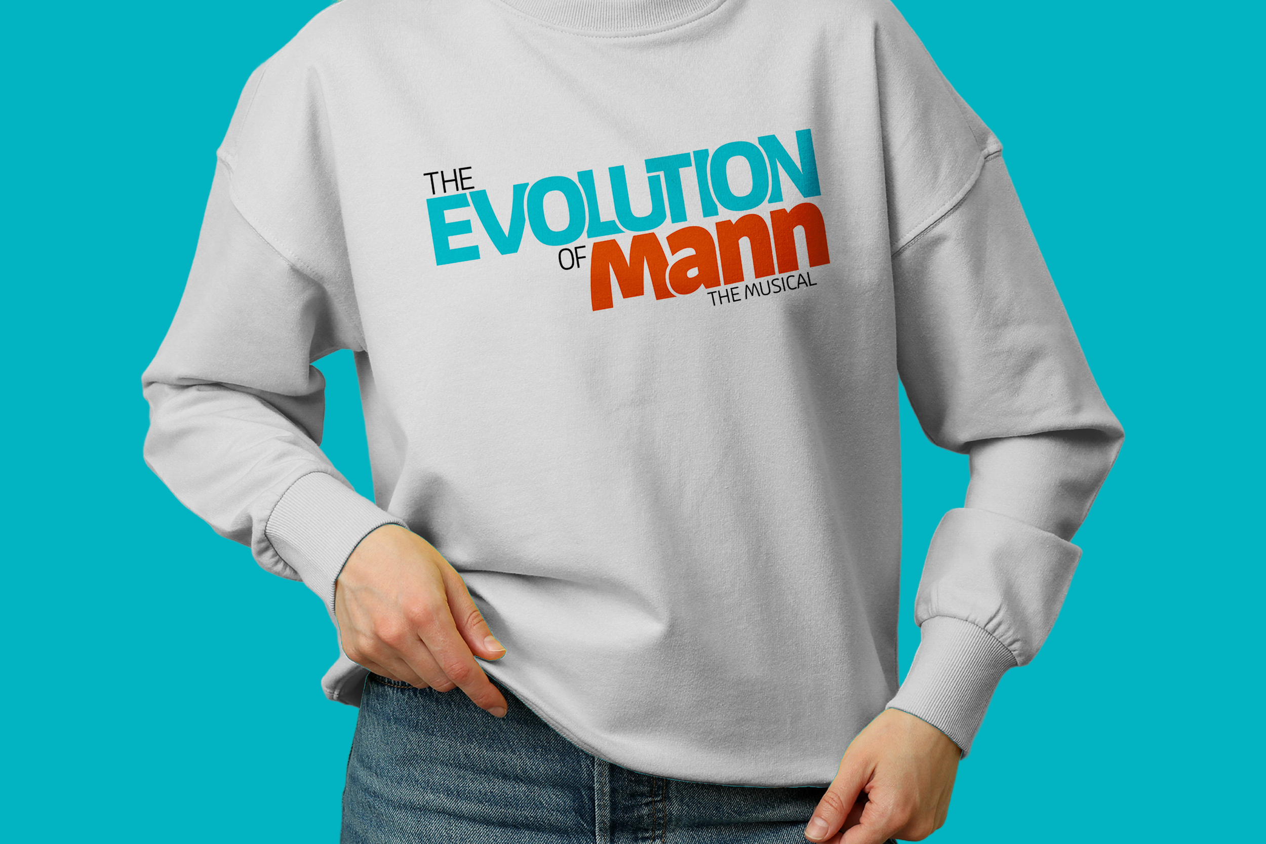 A person wearing a white sweatshirt with colorful text that reads "The Evolution of Man: The Musical" against a turquoise background.