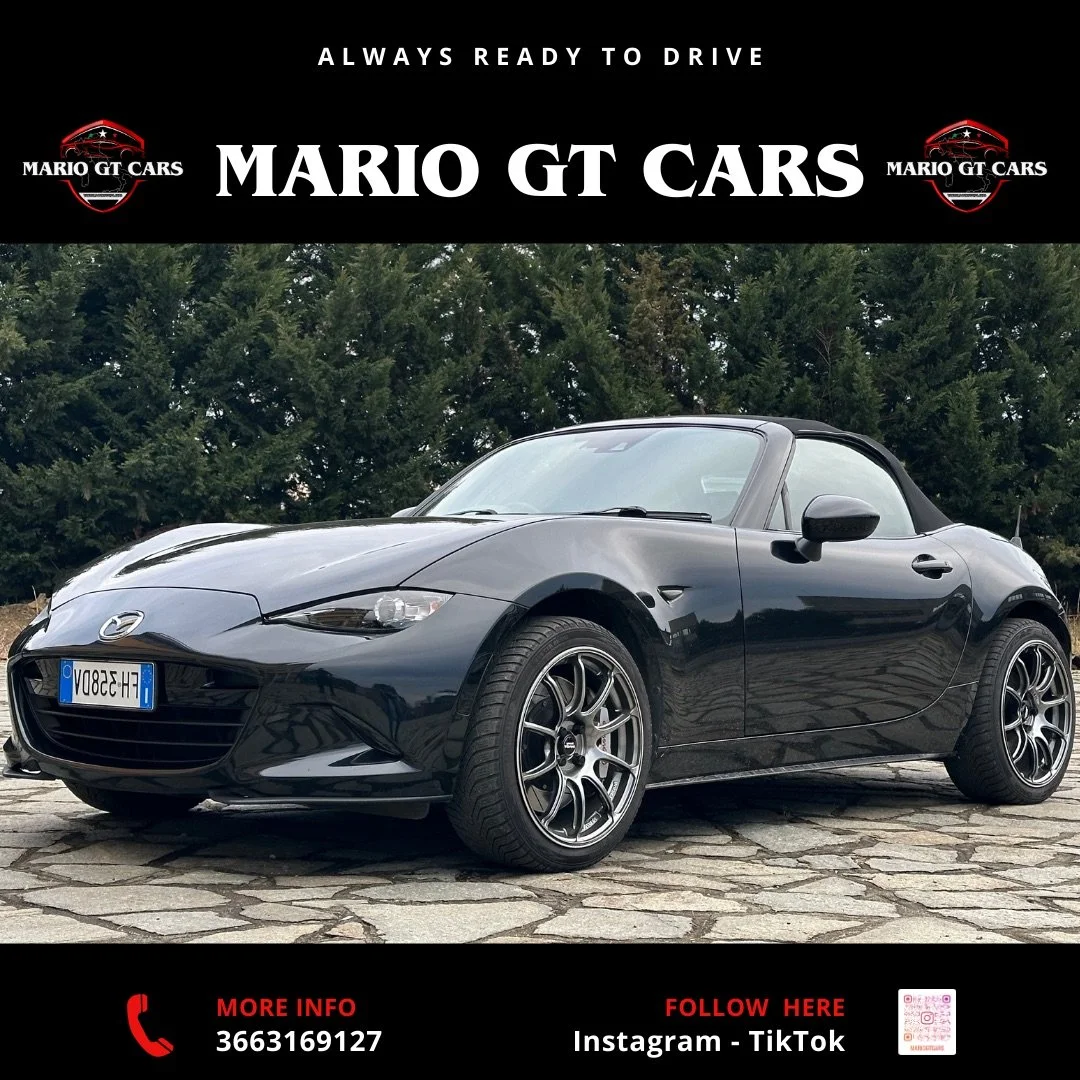 Auto sportiva Mazda MX-5 nera con targa francese, parcheggiata su una strada di pietra logata, con alberi verdi sullo sfondo.