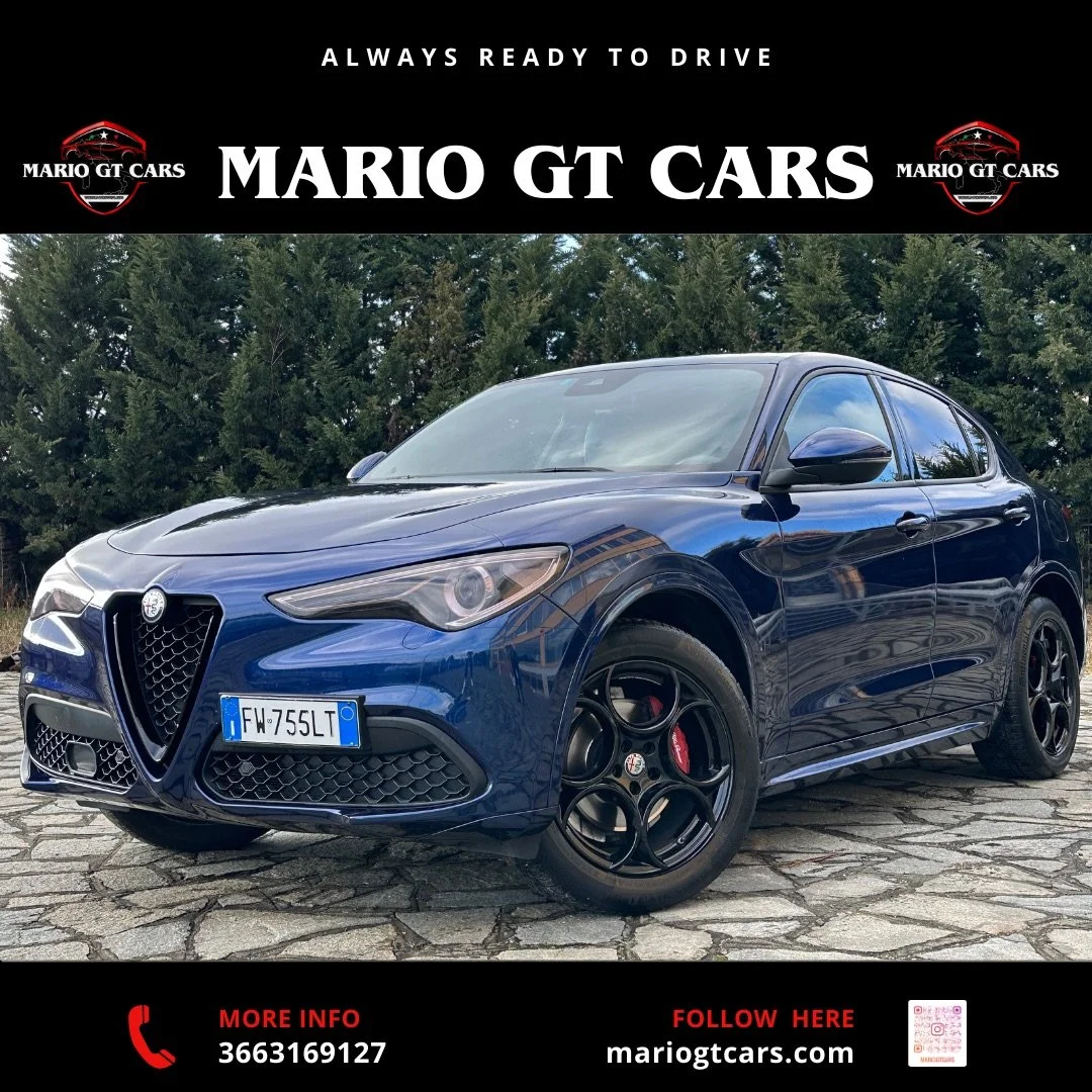 Auto sportiva Alfa Romeo Giulia in colore blu con dettagli neri e cerchi in lega neri, parcheggiata su strada di pietra con alberi sullo sfondo.