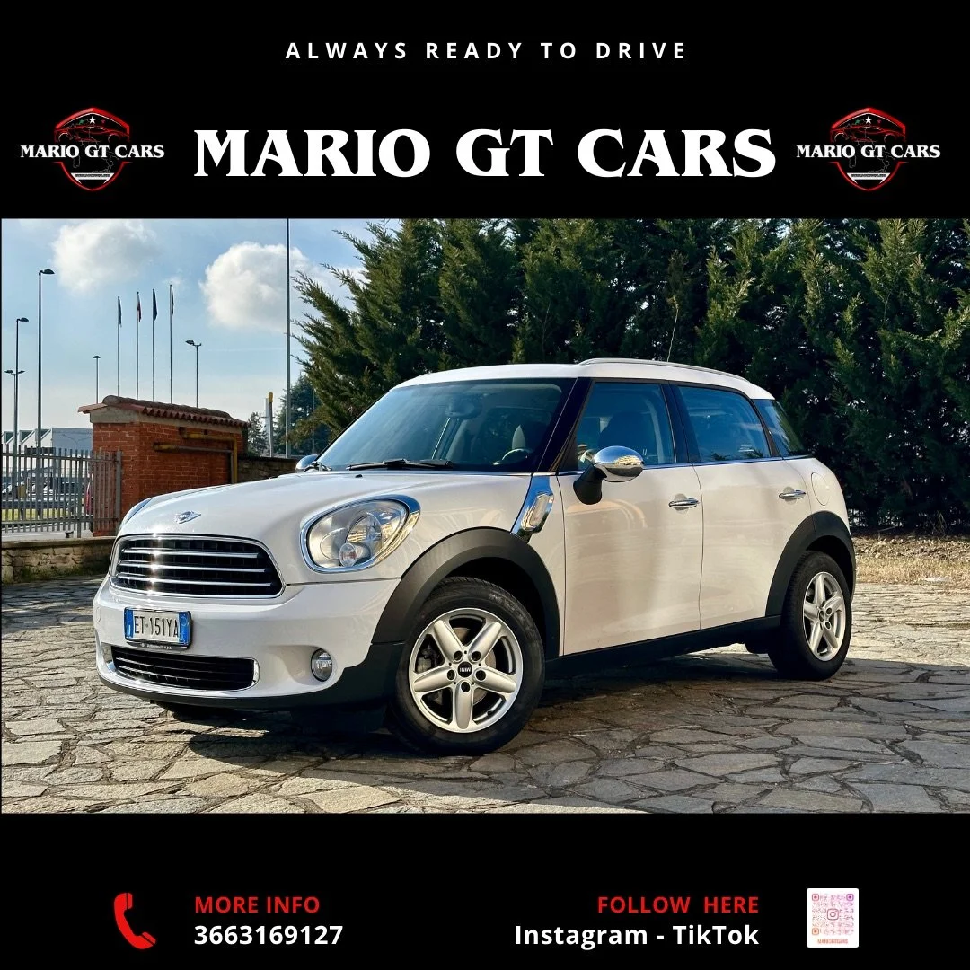 Auto Mini Cooper bianca parcheggiata su una strada di pietra con sfondo di alberi e cielo nuvoloso.