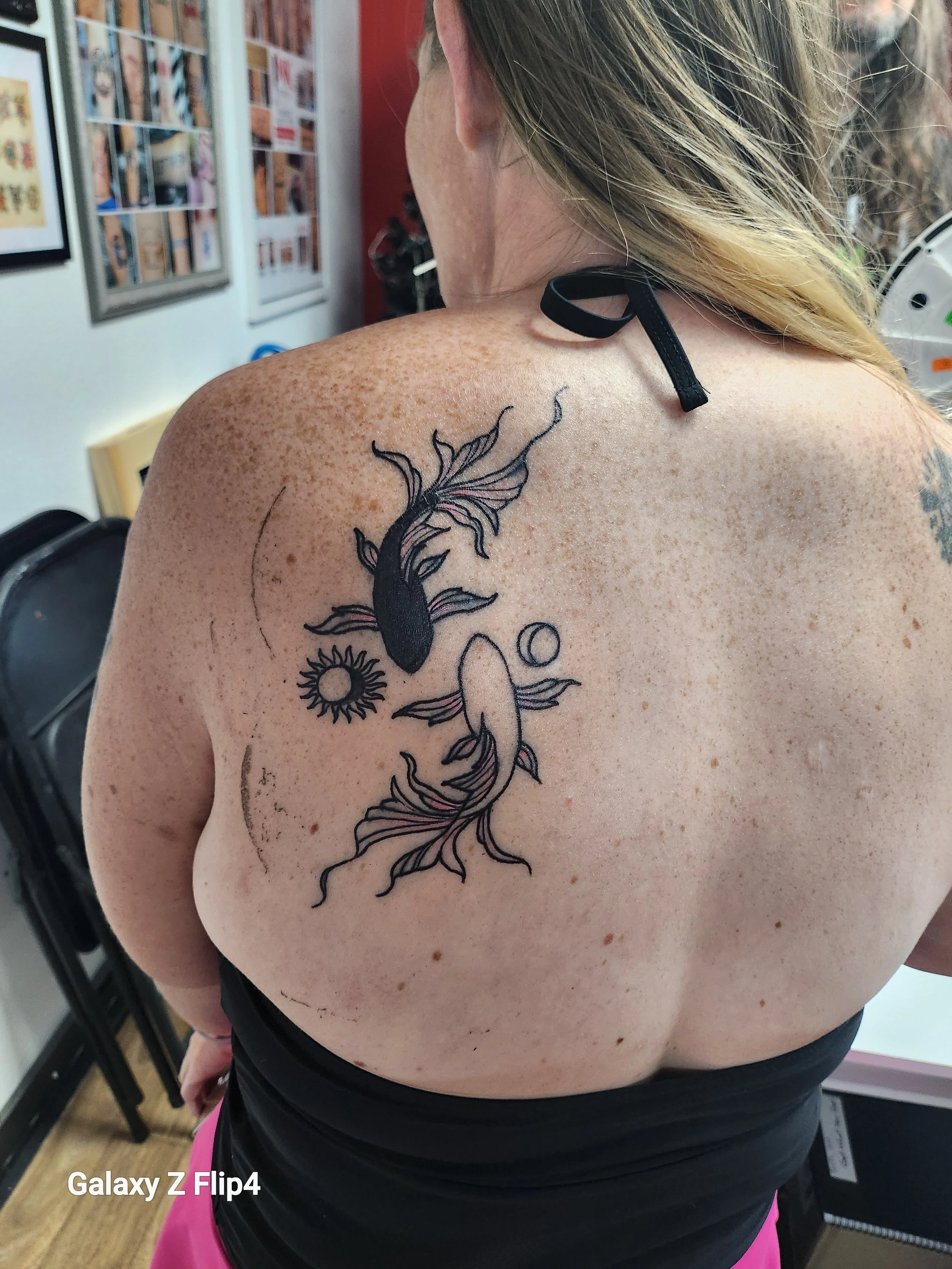 Tattoo of two koi fish swimming towards each other and on the outer sides of each fish there is a moon and sun