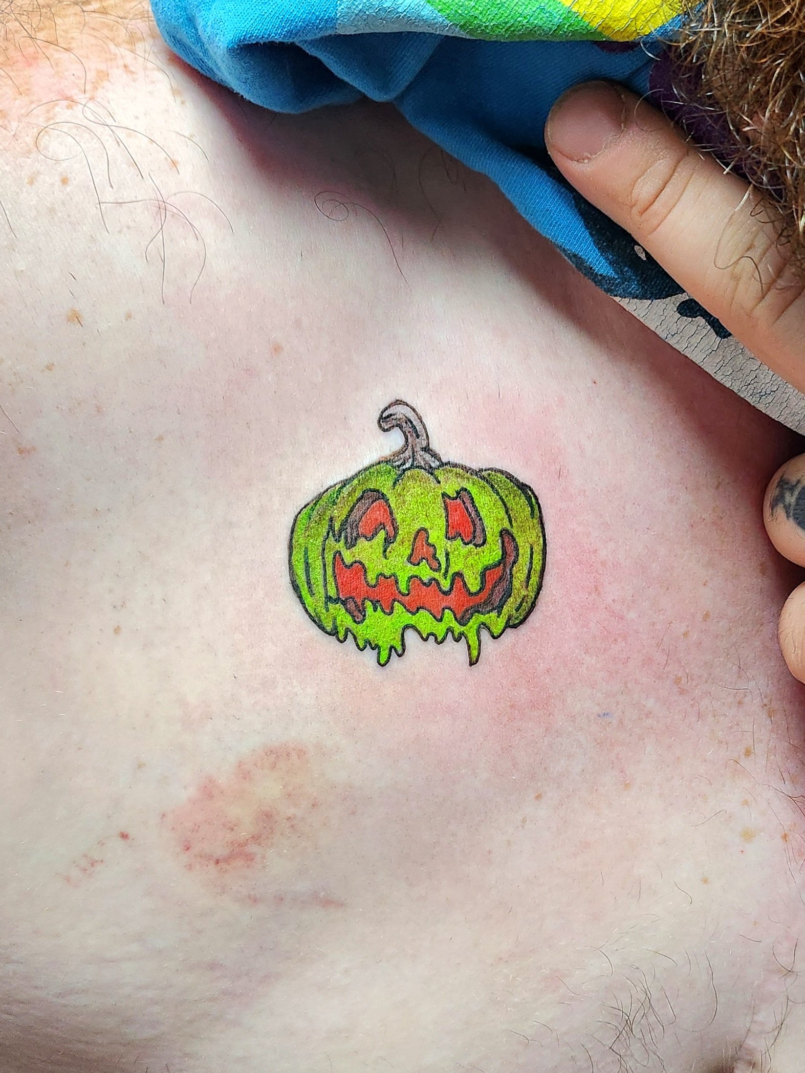 Tattoo of a neon green Jack-O-Lantern with the face in red