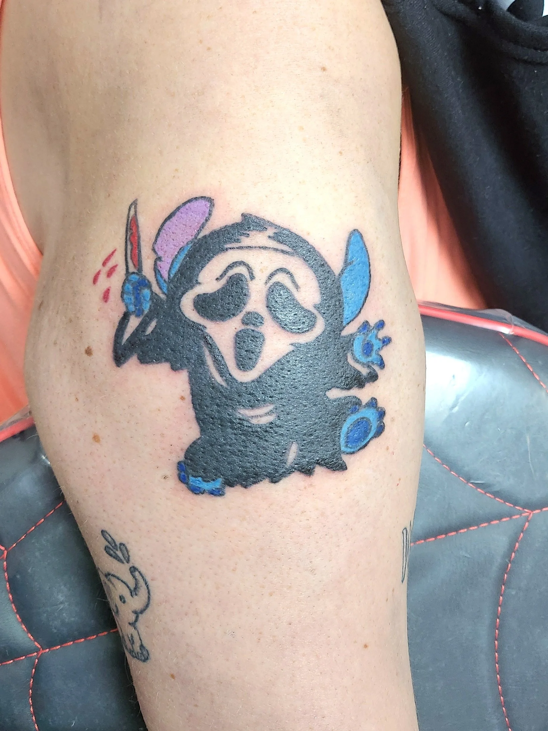 Tattoo of Disney's Stitch dressed in the Ghost Face costume holding a knife with blood dripping from it