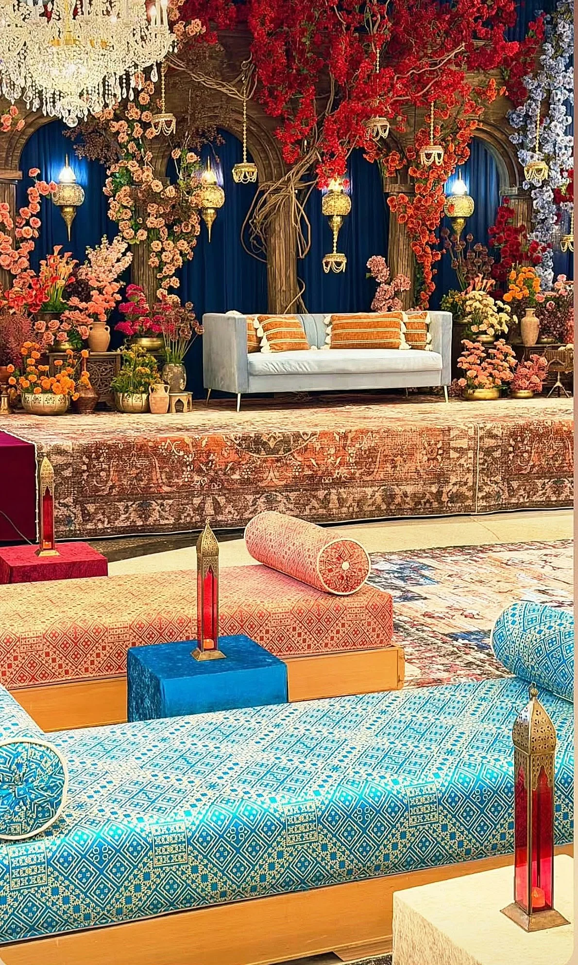Moroccan lounge setup with colorful daybeds, a sofa, patterned rugs, and brass lanterns