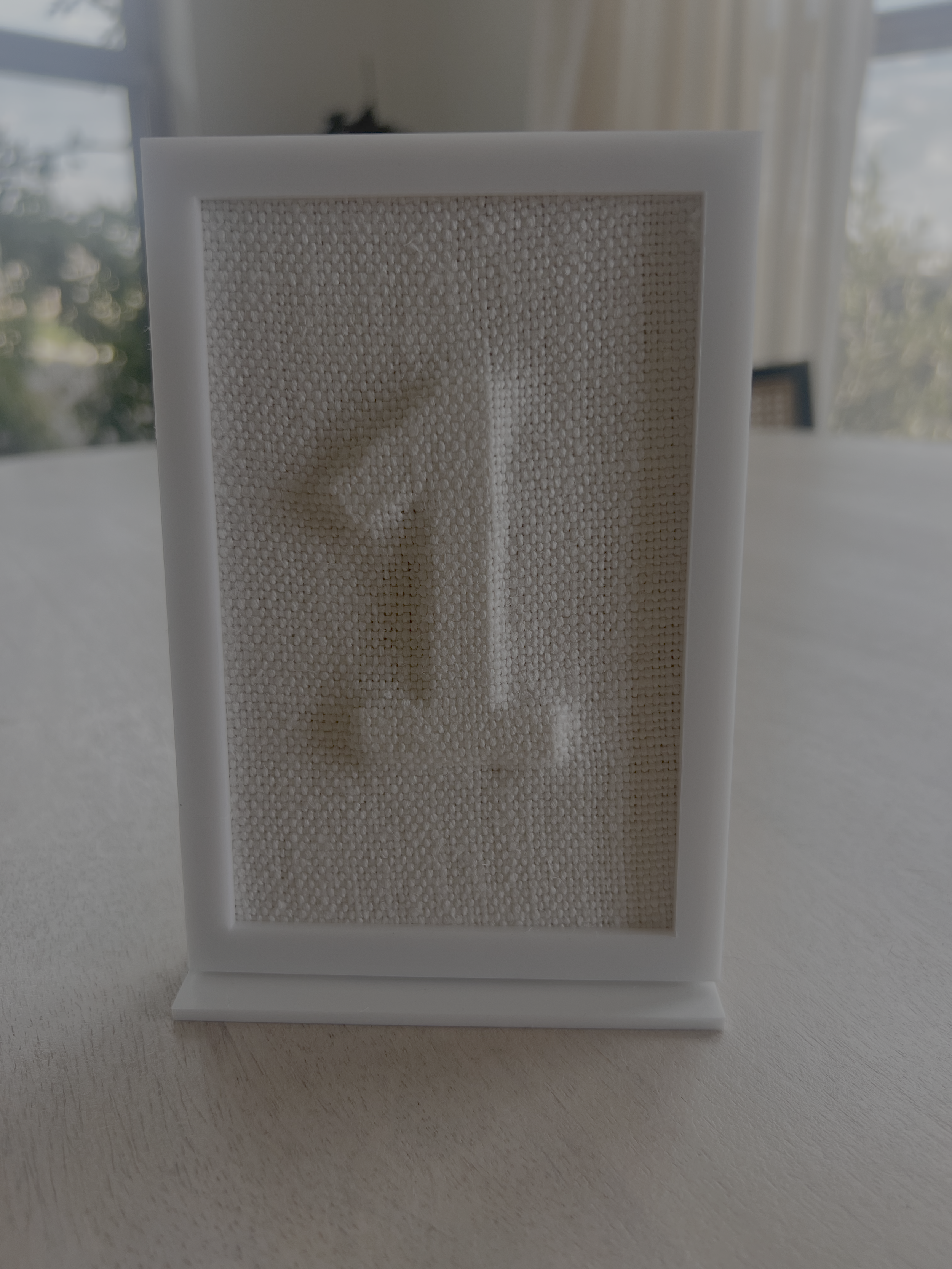White photo frame with a fabric backing on a table.