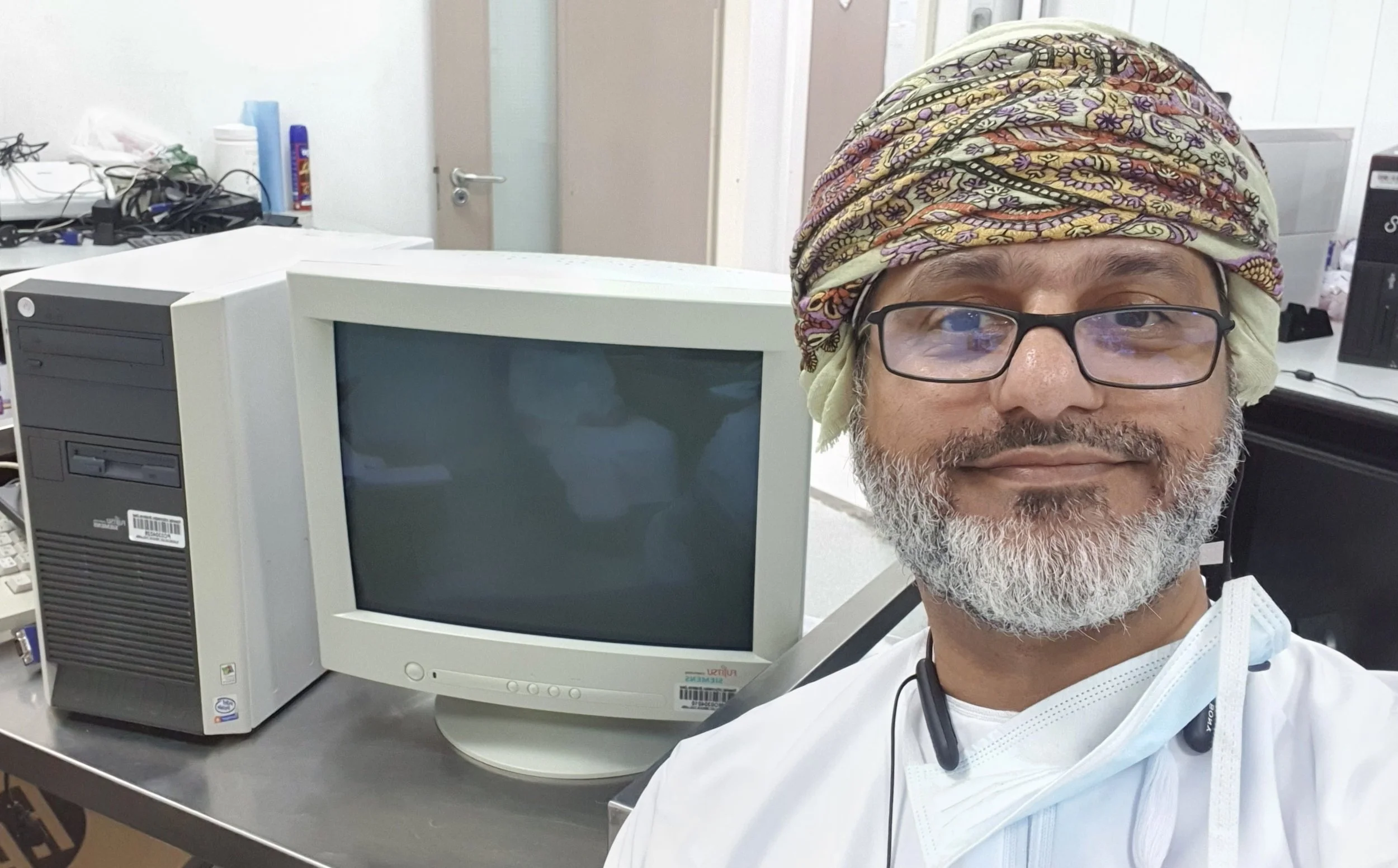 المدرّب إبراهيم البلوشي بجانب حاسوب مكتبي قديم بشاشة CRT في ورشة صيانة أجهزة تقنية المعلومات
