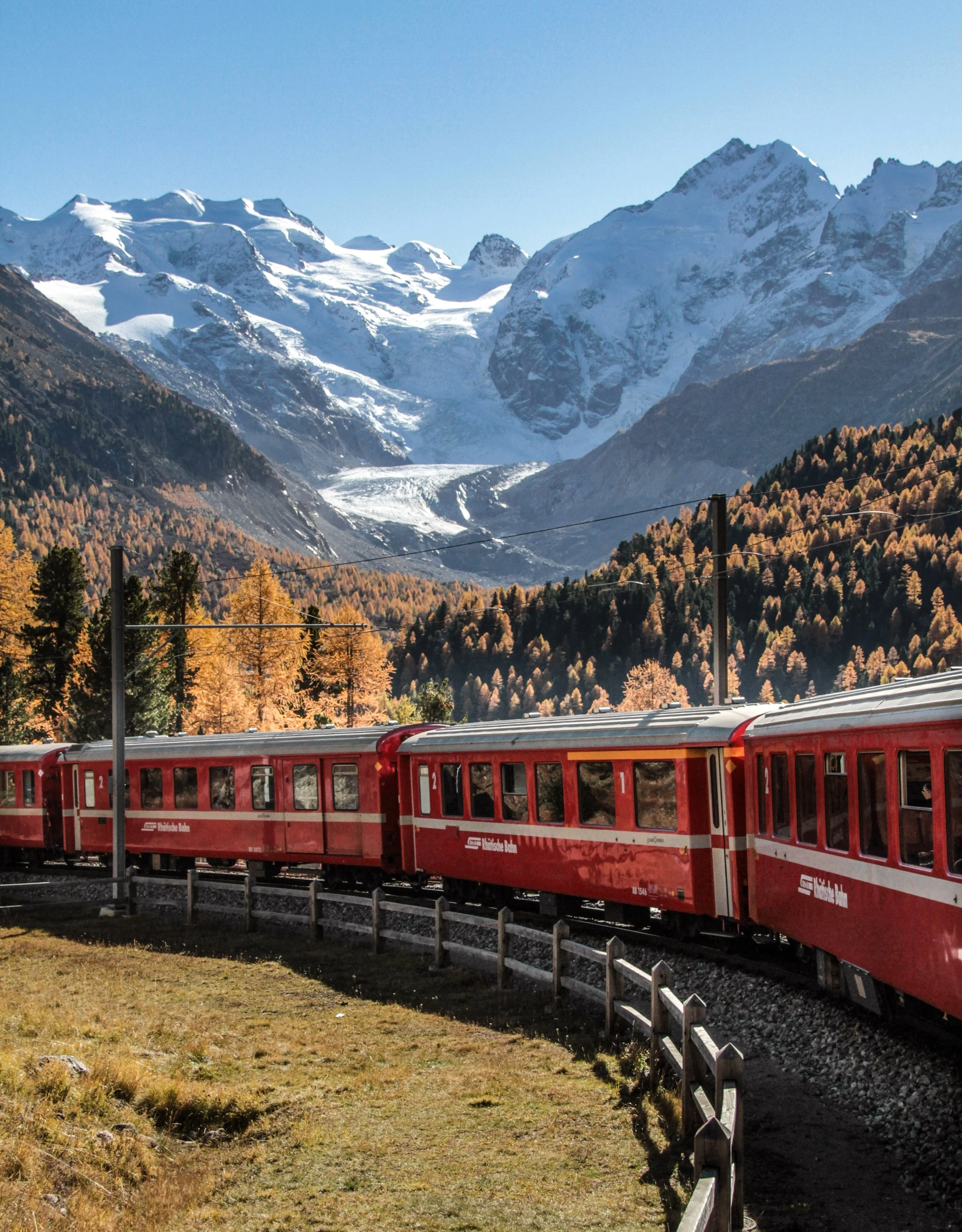 A red train traveling along a snow-covered track in a mountainous, winter landscape.
