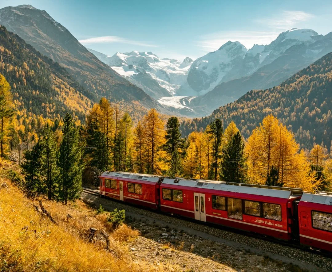 A red train traveling along a snow-covered track in a mountainous, winter landscape.