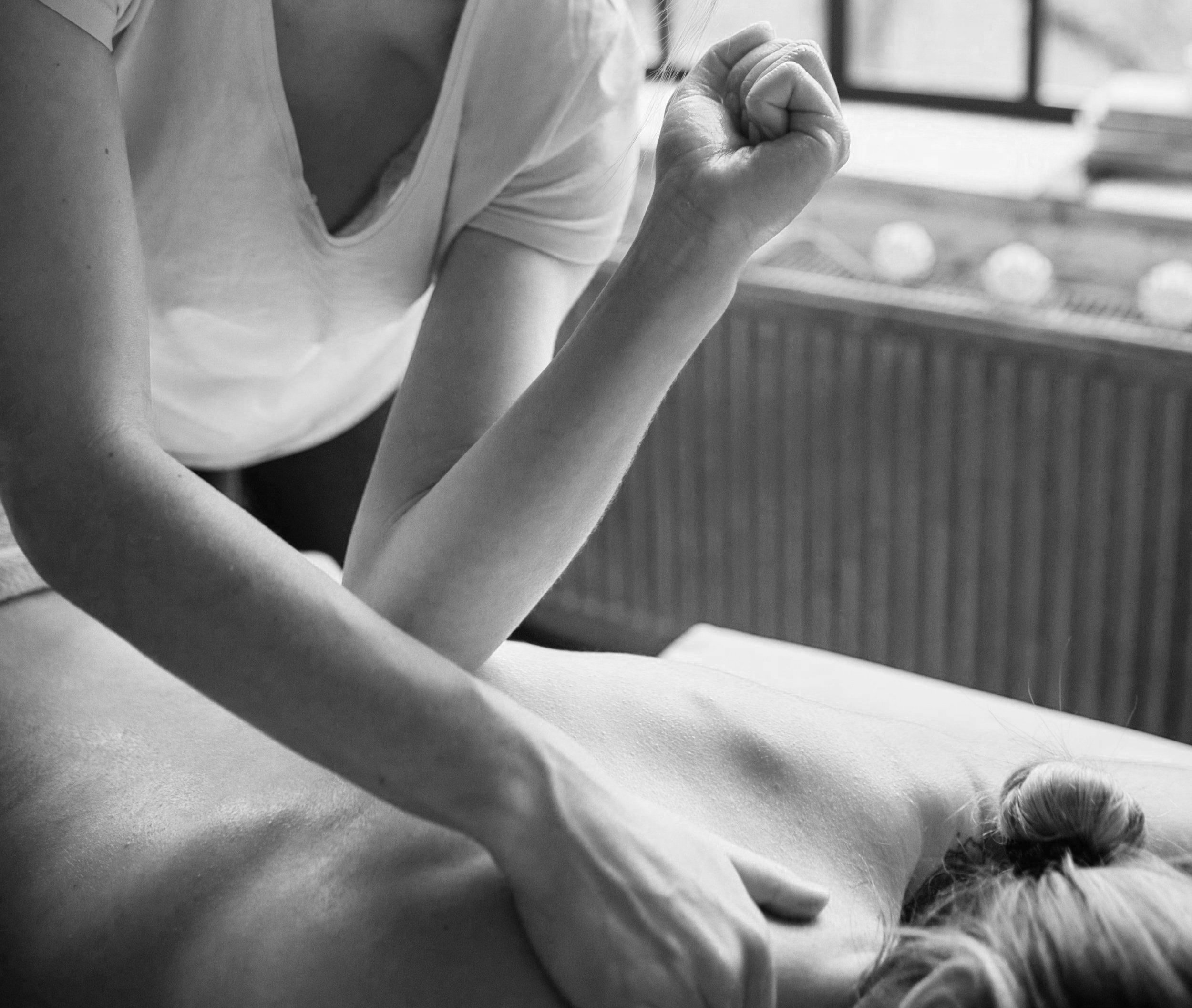 A person receiving a massage on their back from a massage therapist in a wellness setting, black and white photo.