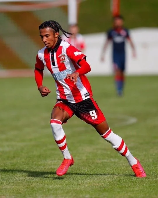 Soccer player in red and white striped jersey running on the field during a game.