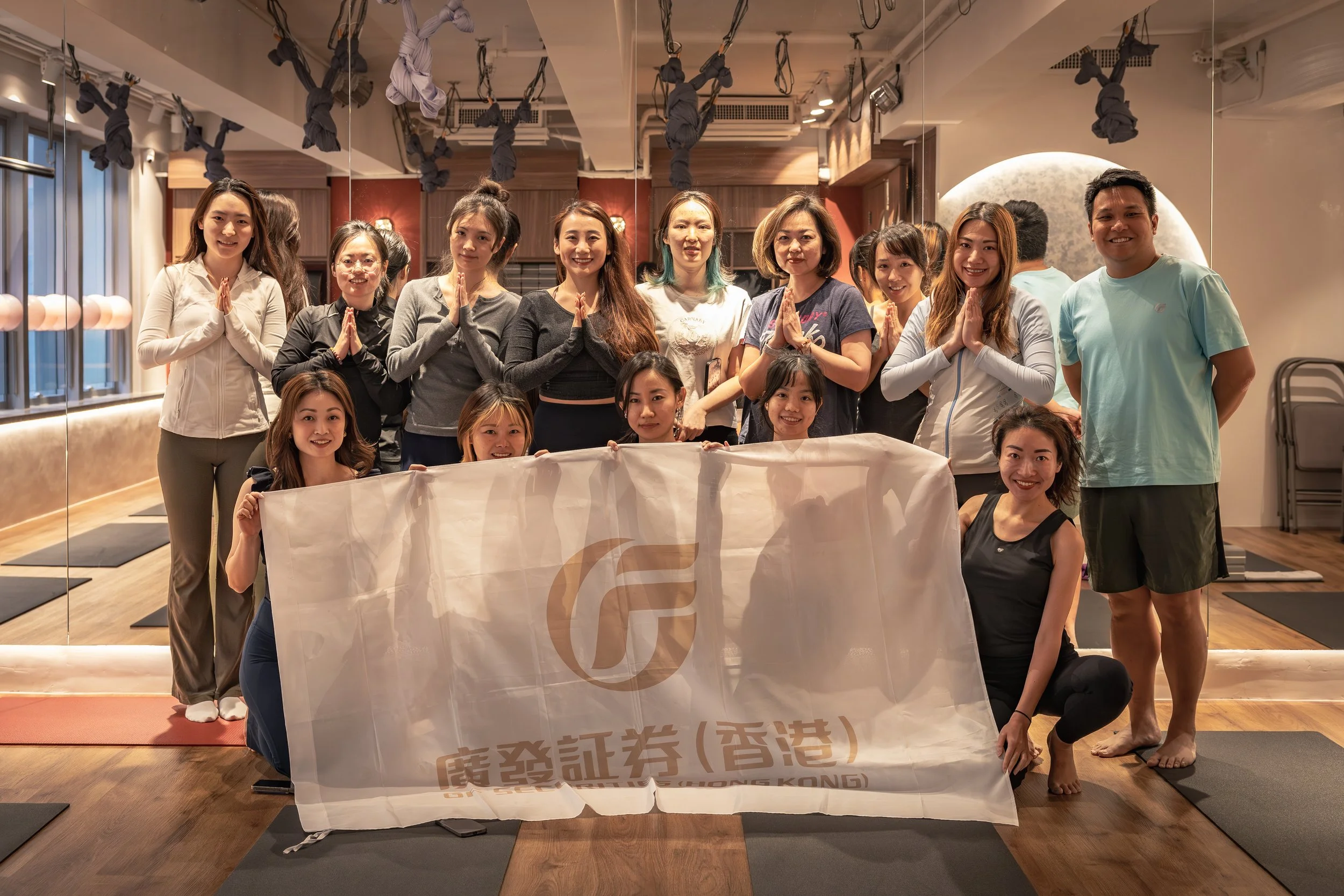 Corporate yoga class organized by IMAYOGI – GF Holdings team photo with company banner promoting workplace wellness in Hong Kong and Wan Chai.