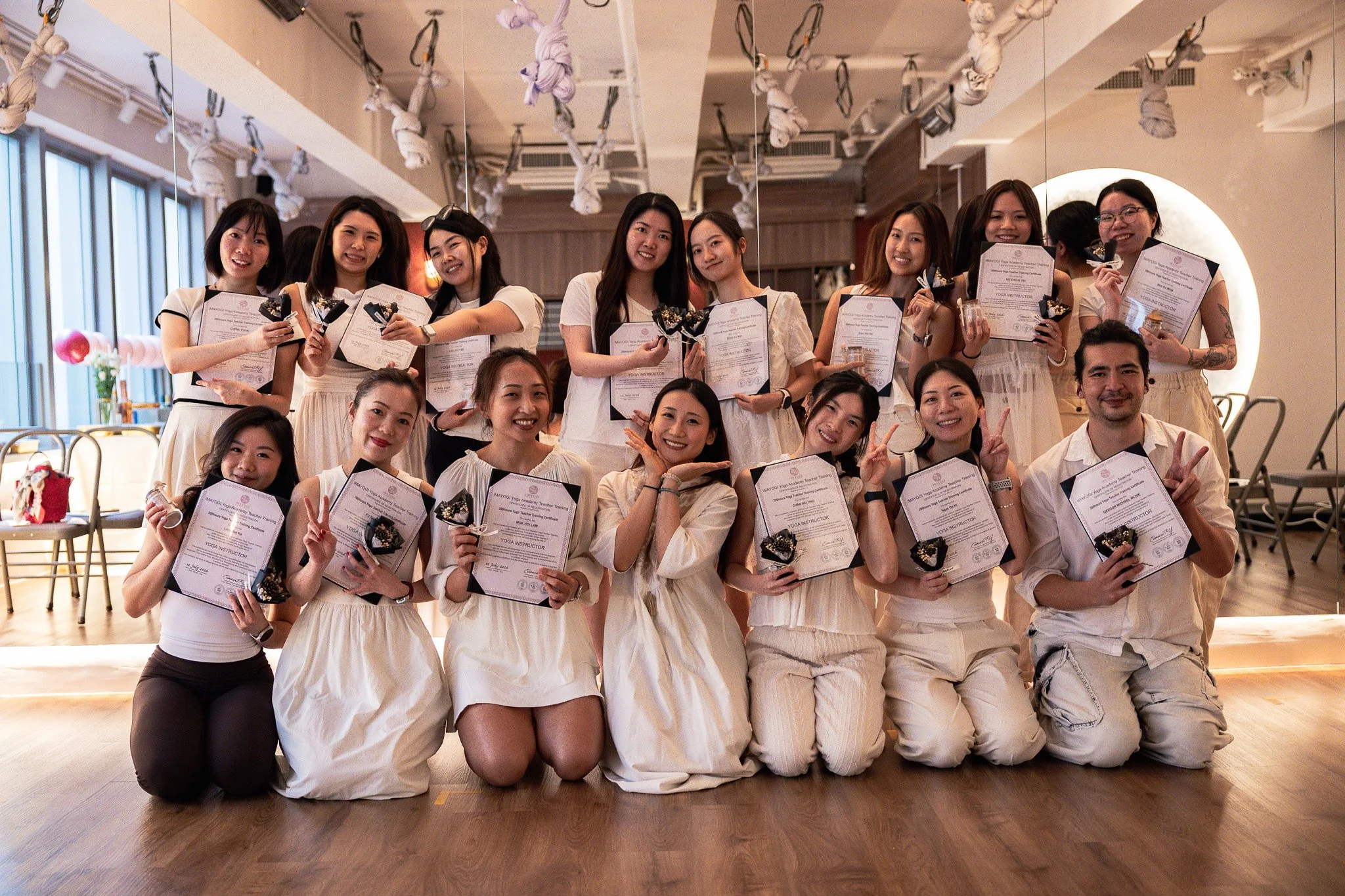 Group of women holding certificates and flowers, taking a selfie together in an outdoor setting.