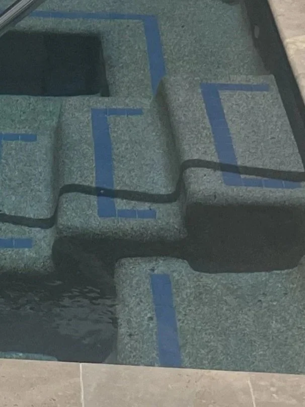 A hot tub or pool with built-in seating and steps, with blue tile accents and water visible at the edges.