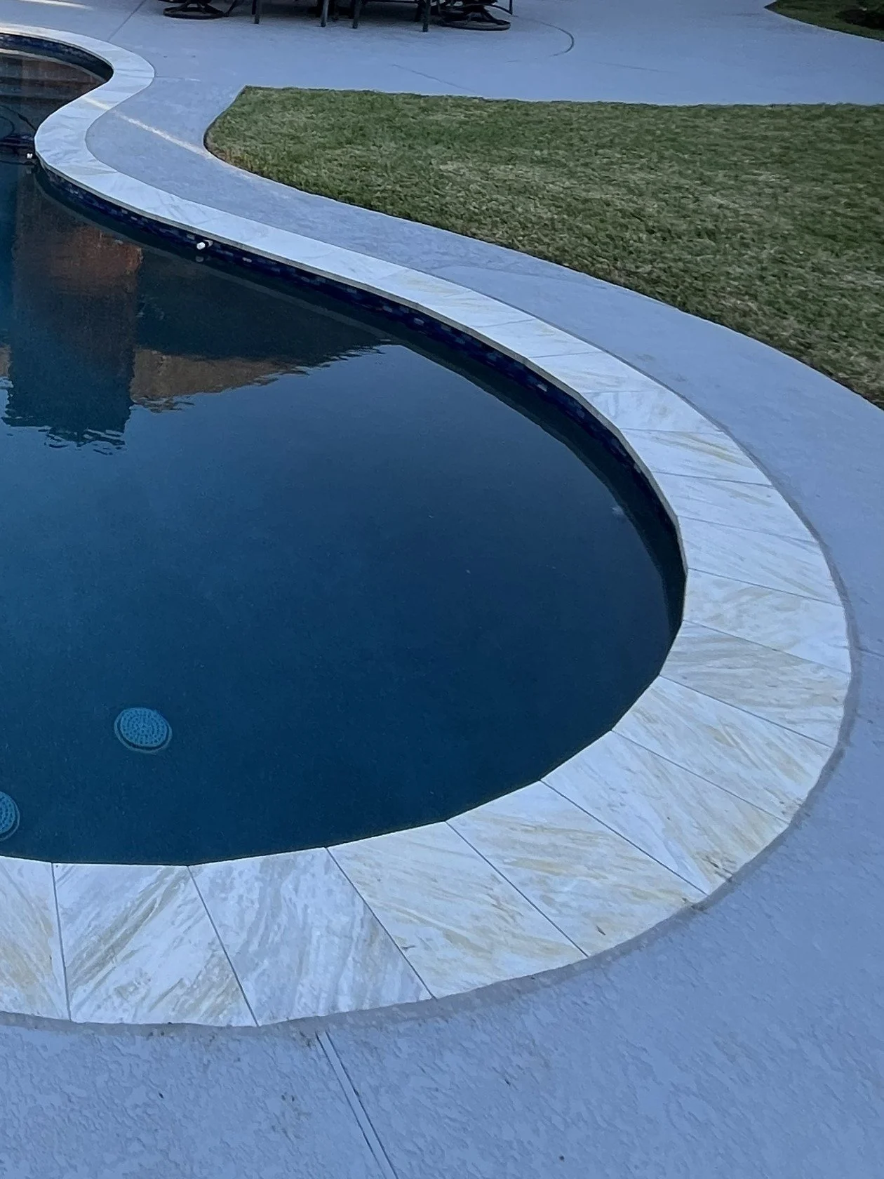 A swimming pool with a white tiled border and a grass area nearby.