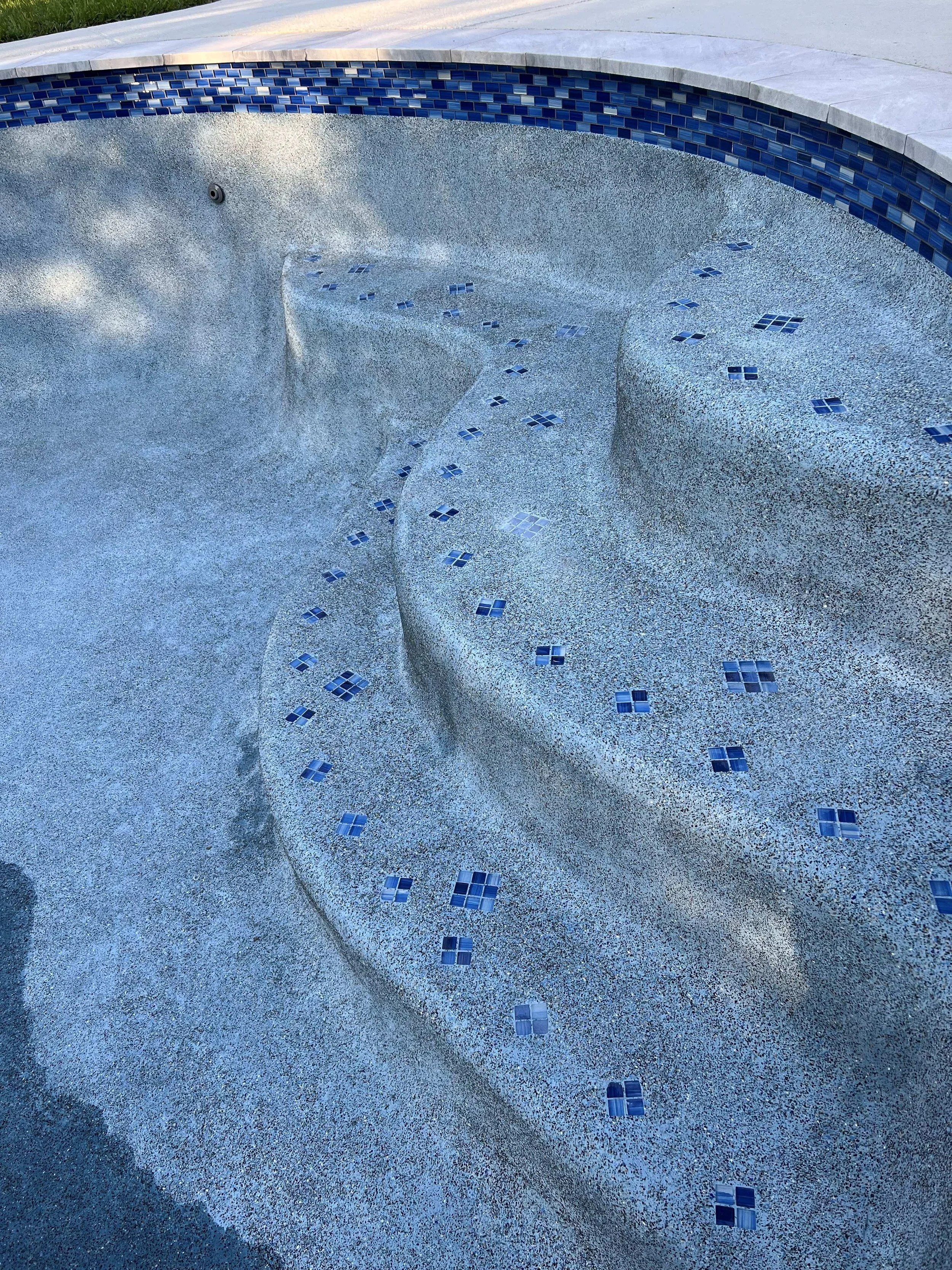Empty swimming pool with a textured, speckled surface and blue tile accents along the top edge.