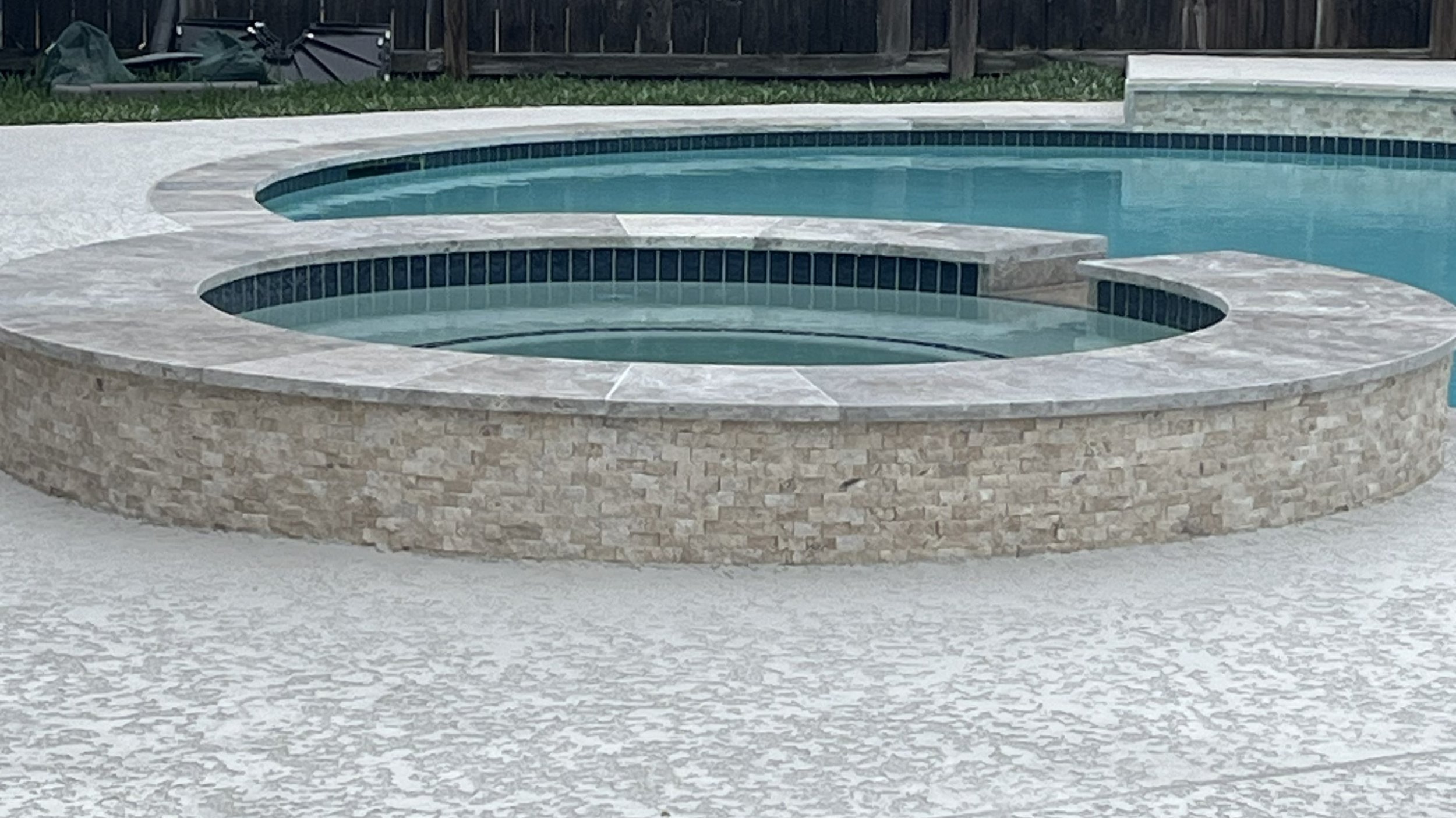Backyard swimming pool featuring new NPT Stonescapes Mini-pebble plaster in White Osprey, new travertine coping, and new NPT Moonscapes waterline tile in Steel Blue, a new spray deck over Carvestone.