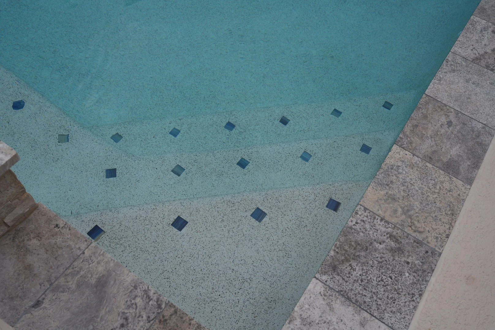 Underwater pool entry steps with blue square accent tiles set into a light pebble interior finish.