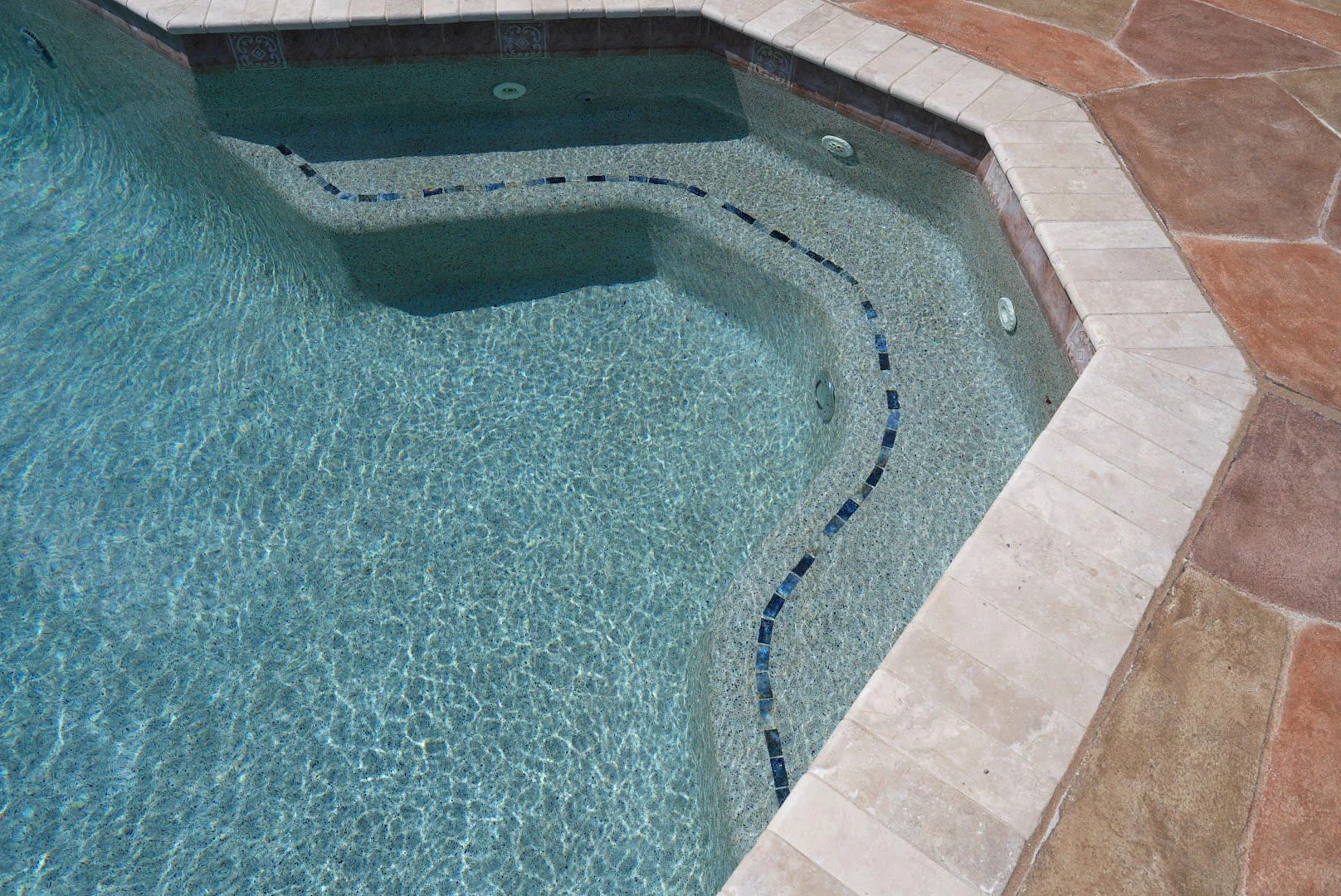 Curved pool bench with blue accent tile and textured pool finish at Carrington Oaks