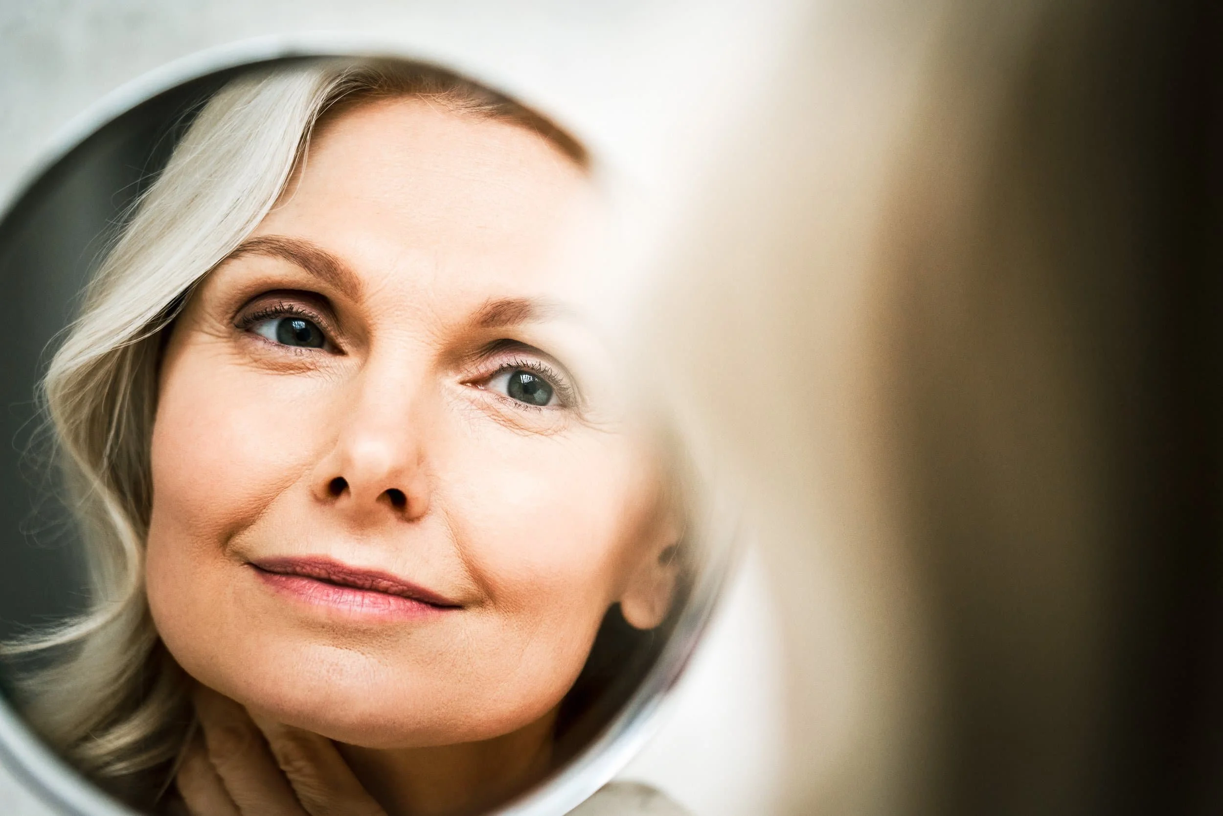 middle aged woman admiring her face in the mirror after a beauty treatment