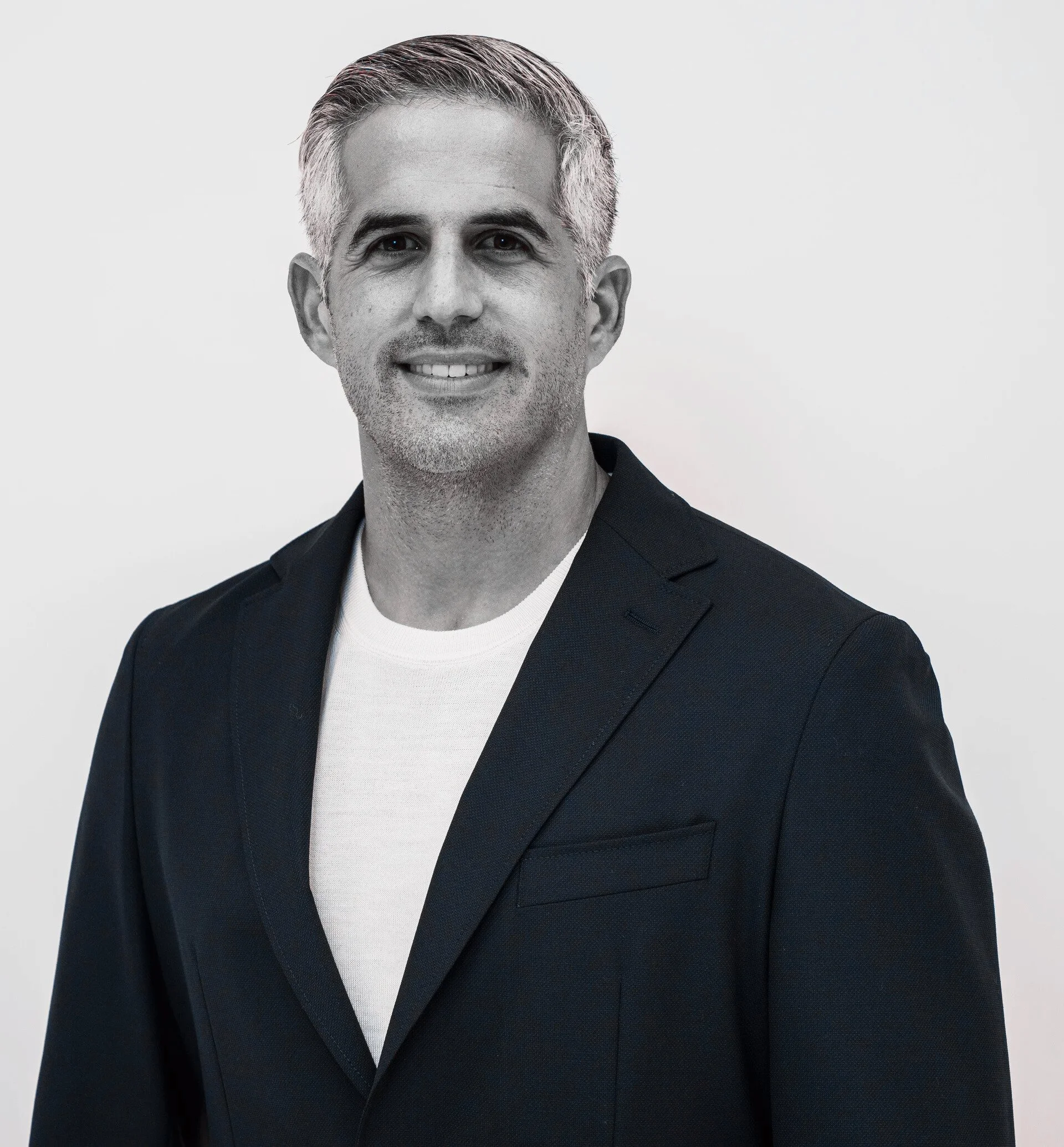 Black and white portrait of a middle-aged man with short, gray hair, wearing a dark blazer and a white shirt, smiling slightly, against a plain backdrop.