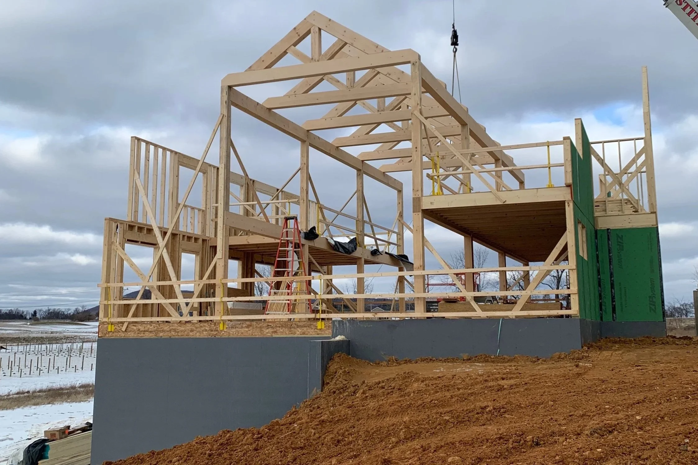 Wood framing of a house under construction on a concrete foundation, with cloudy skies in the background.