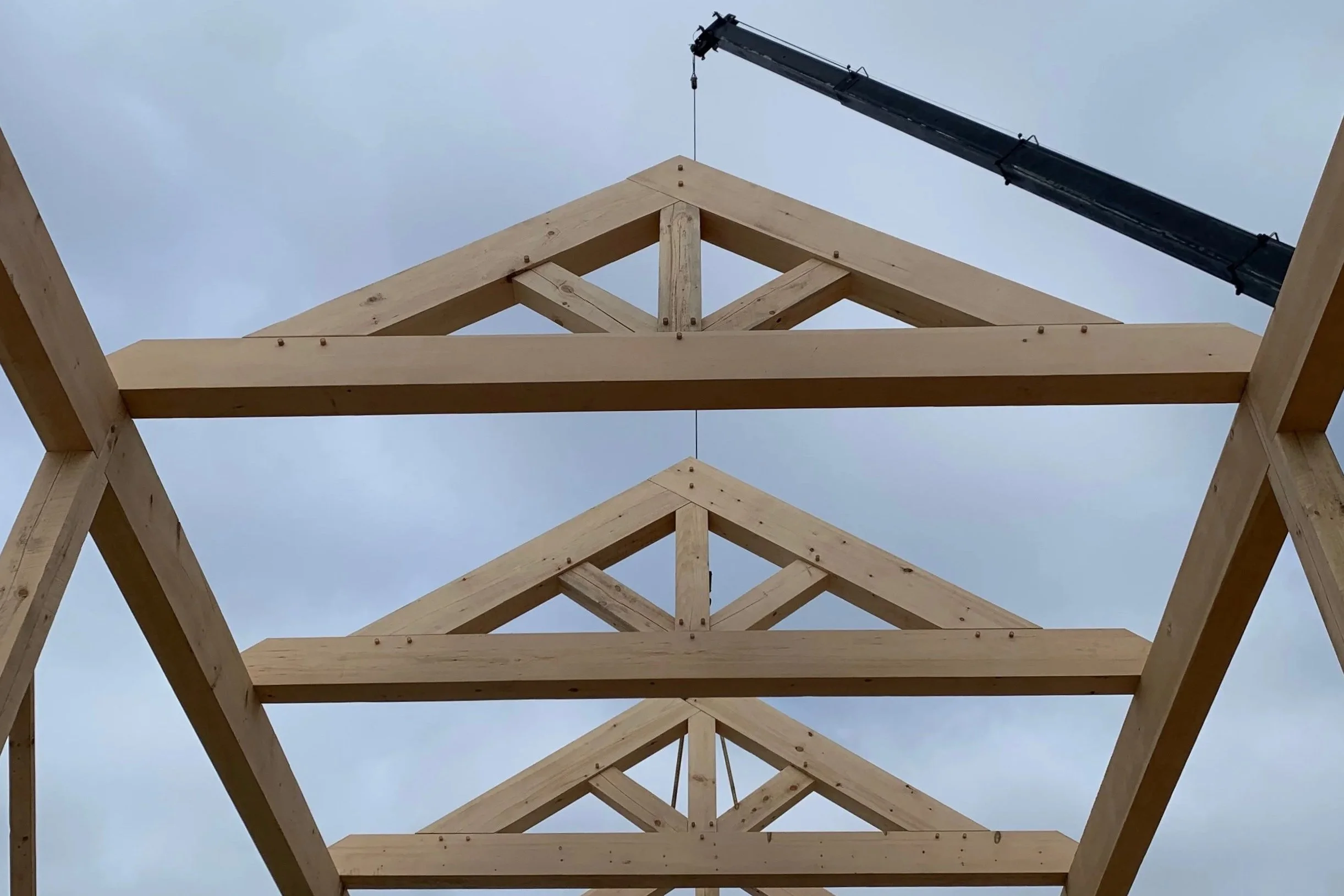 Wooden roof trusses under construction with a crane lifting equipment in the background.