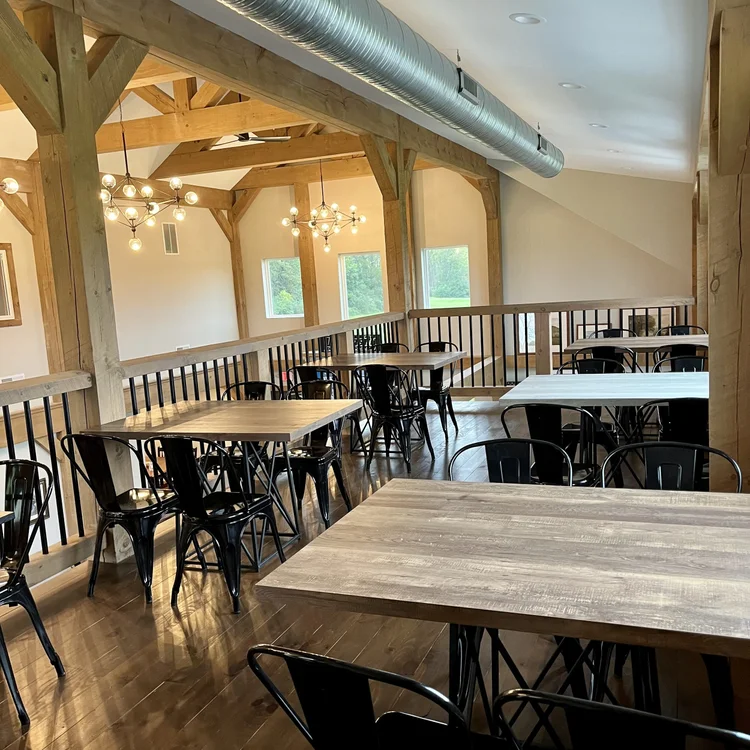 Interior of a dining area with wooden tables and black chairs, wooden beams, modern chandeliers, and windows providing outside views.