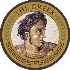A circular emblem featuring a profile illustration of a woman with short, curly hair and earrings. The emblem has a gold background with a green laurel wreath on top and decorative Greek key pattern on the bottom border. The text reads 'THE GREEK' at the top.