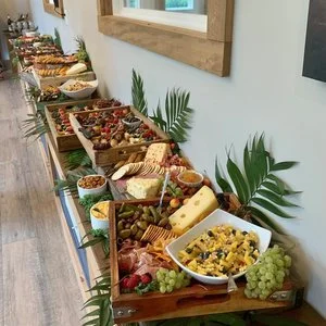 A long table set with a variety of food, including cheese, grapes, dips, bread, and fresh fruit, arranged as a buffet.