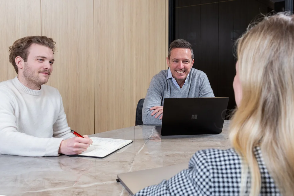 Businessman using a laptop during a meeting at a marble table, colleagues seated nearby