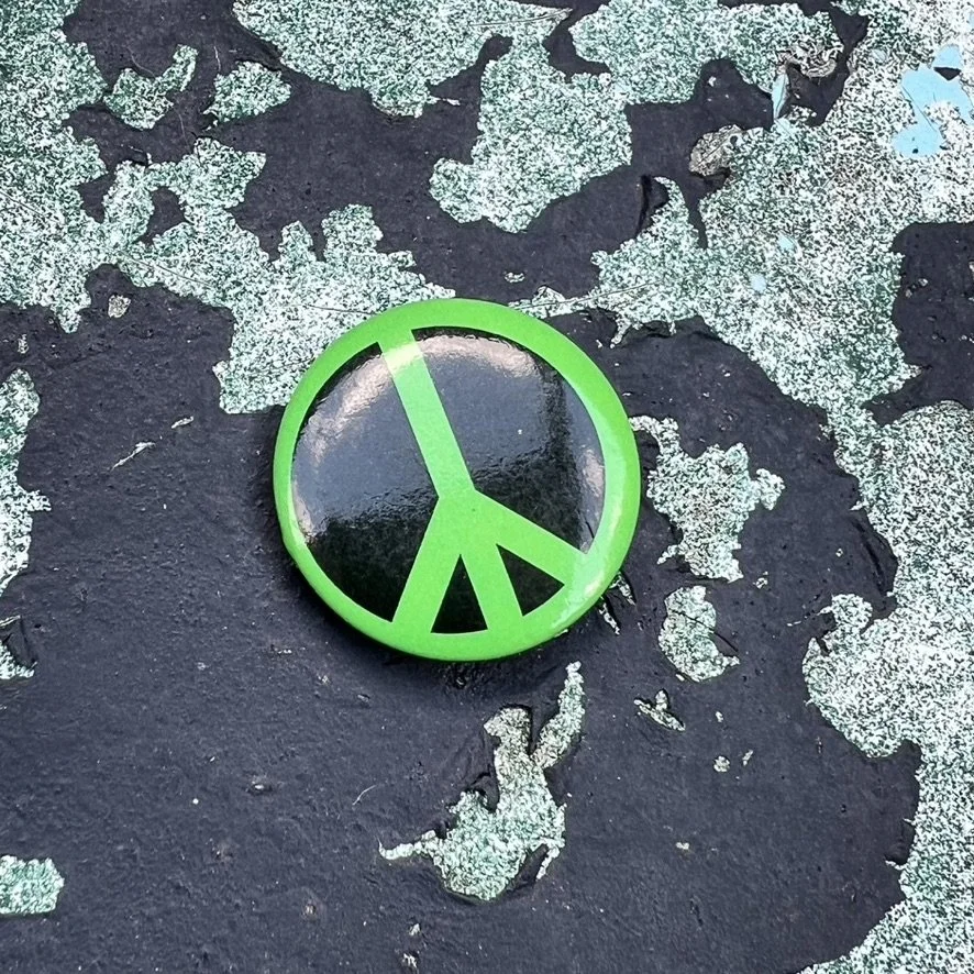 Small button with black peace sign on green background