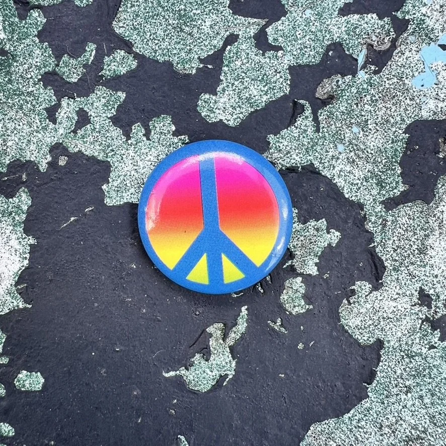 Small button with bright blue peace sign on rainbow background