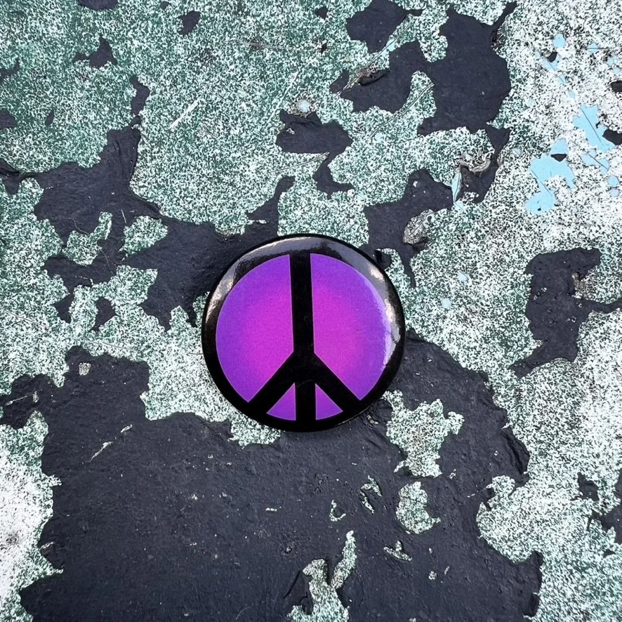 Small button with black peace sign on purple background