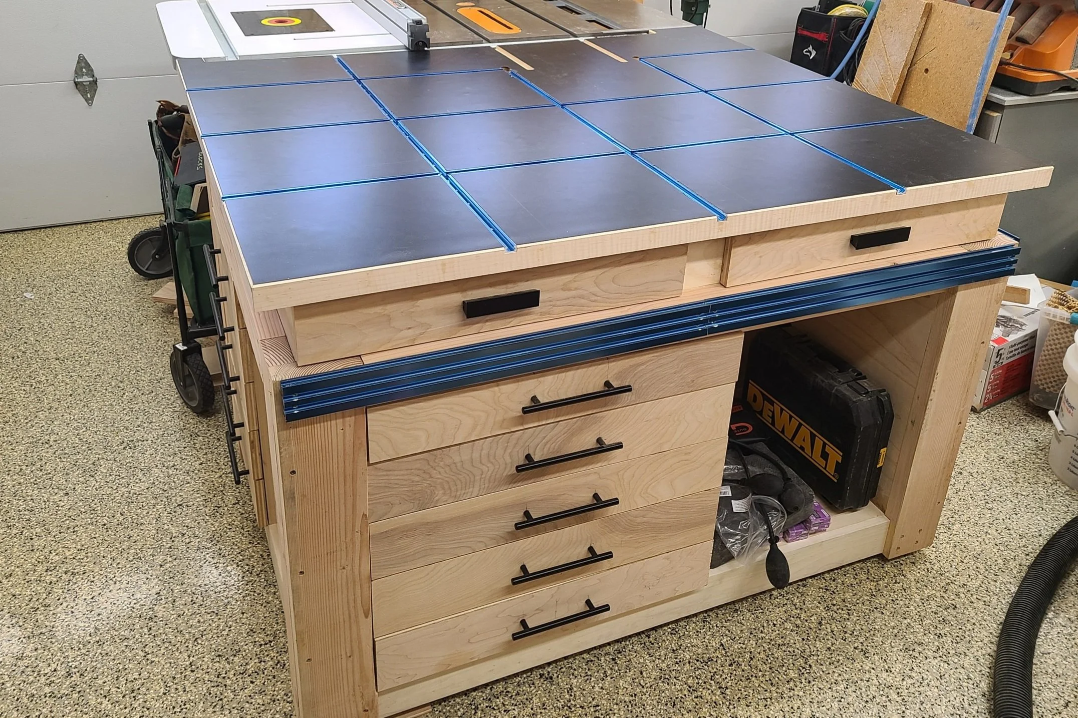 Workshop table saw station with integrated storage drawers and tools.