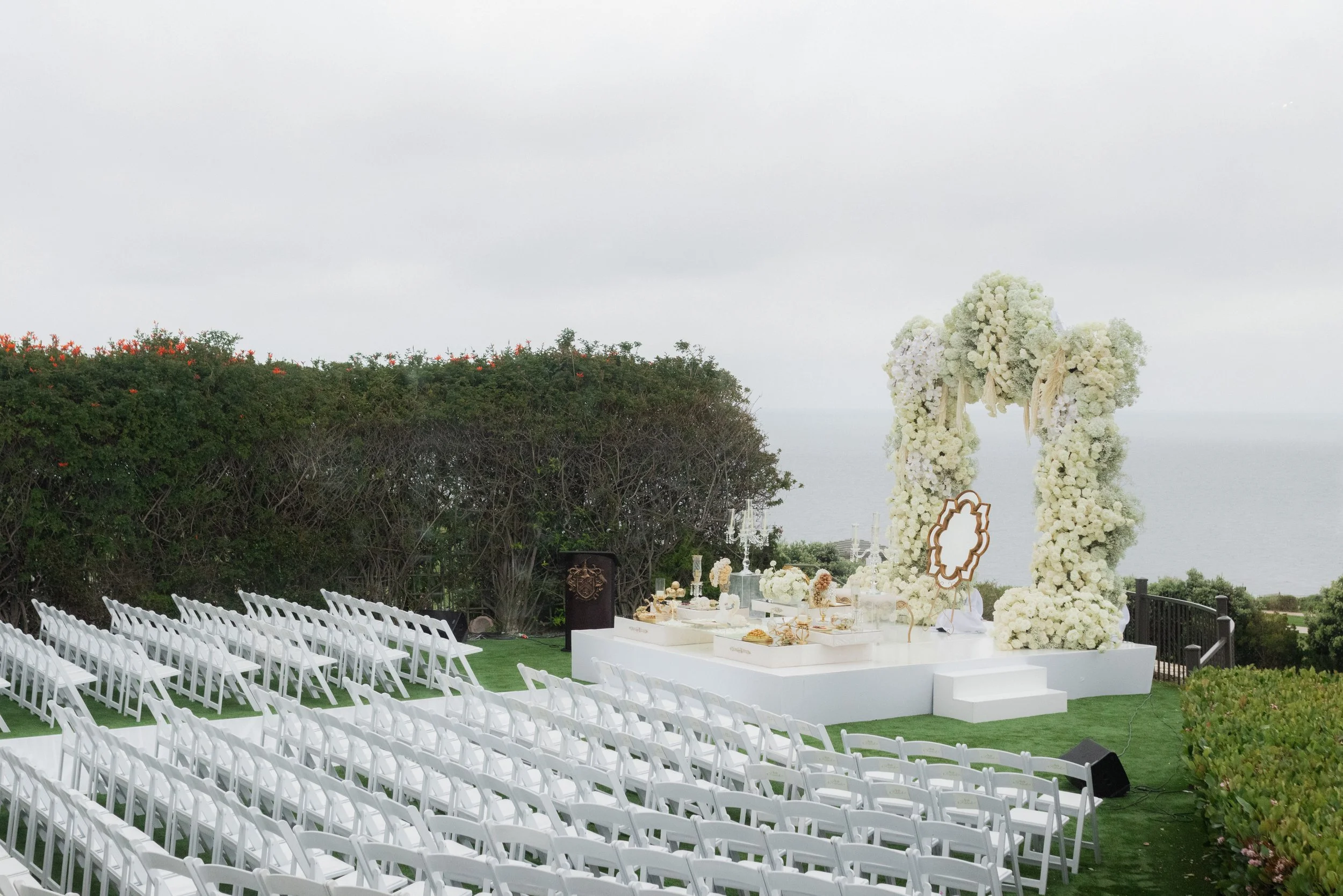 Outdoor wedding ceremony setup with white chairs and floral arch overlooking the ocean.
