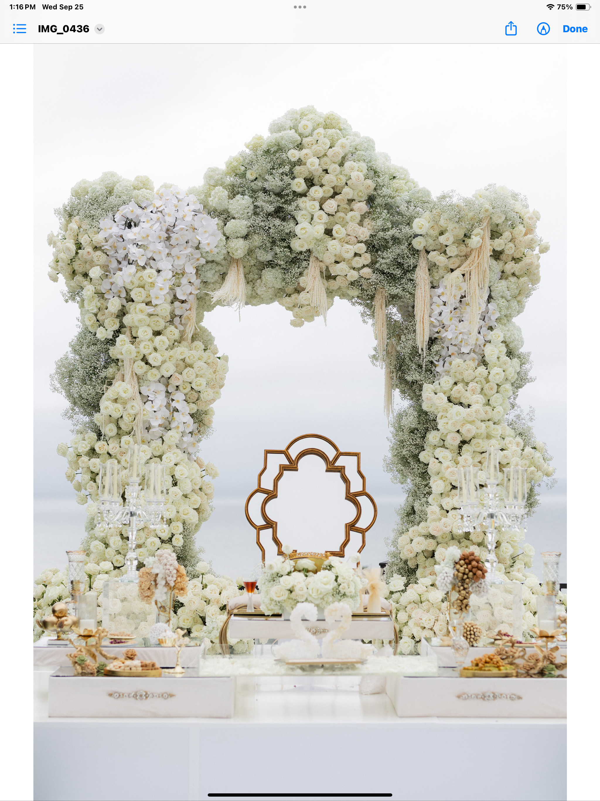 Luxurious floral arch of white roses and baby's breath with decorative table setup, including a mirror, candlesticks, and elegant swan display.