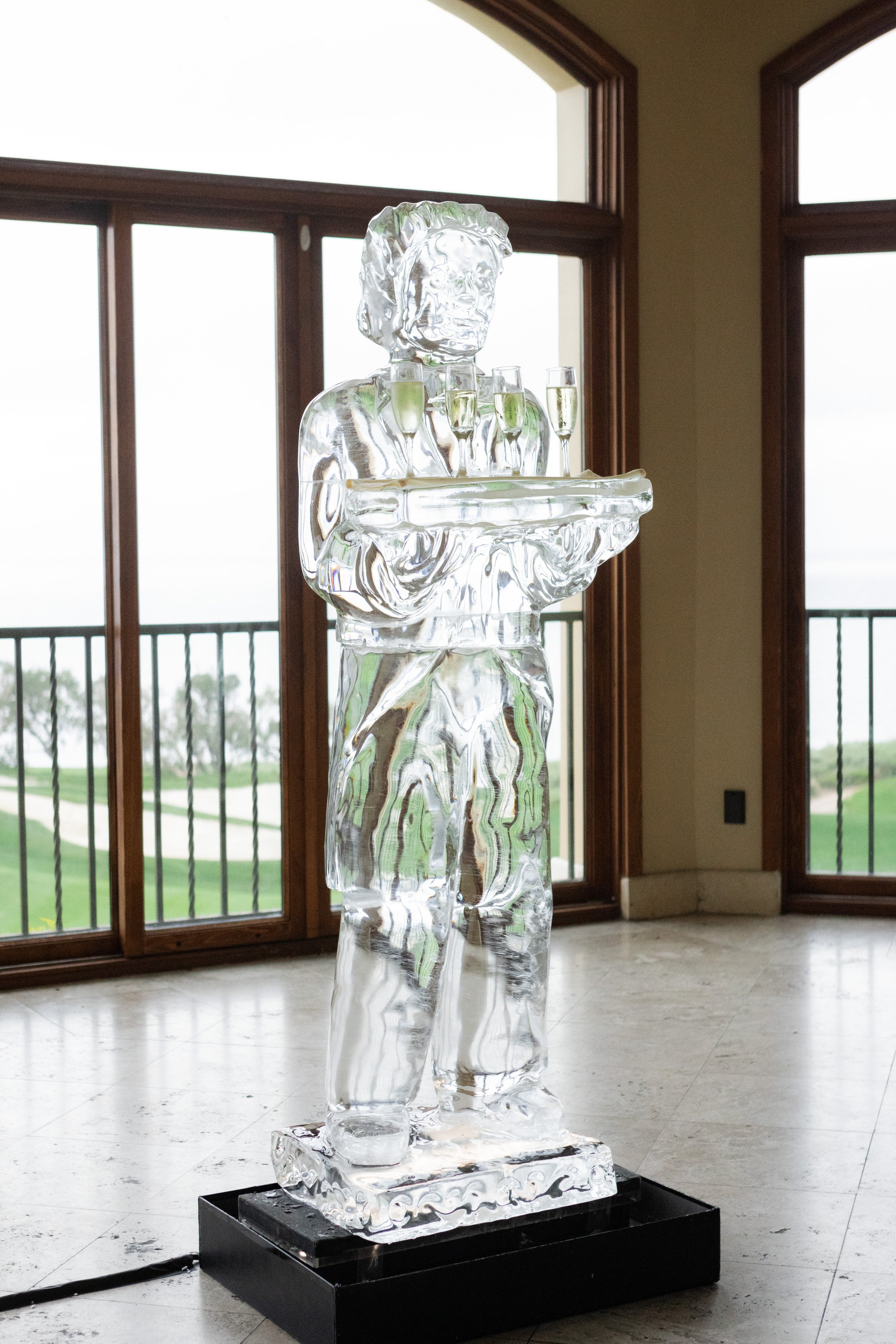 Ice sculpture of a waiter holding a tray with champagne glasses indoors.