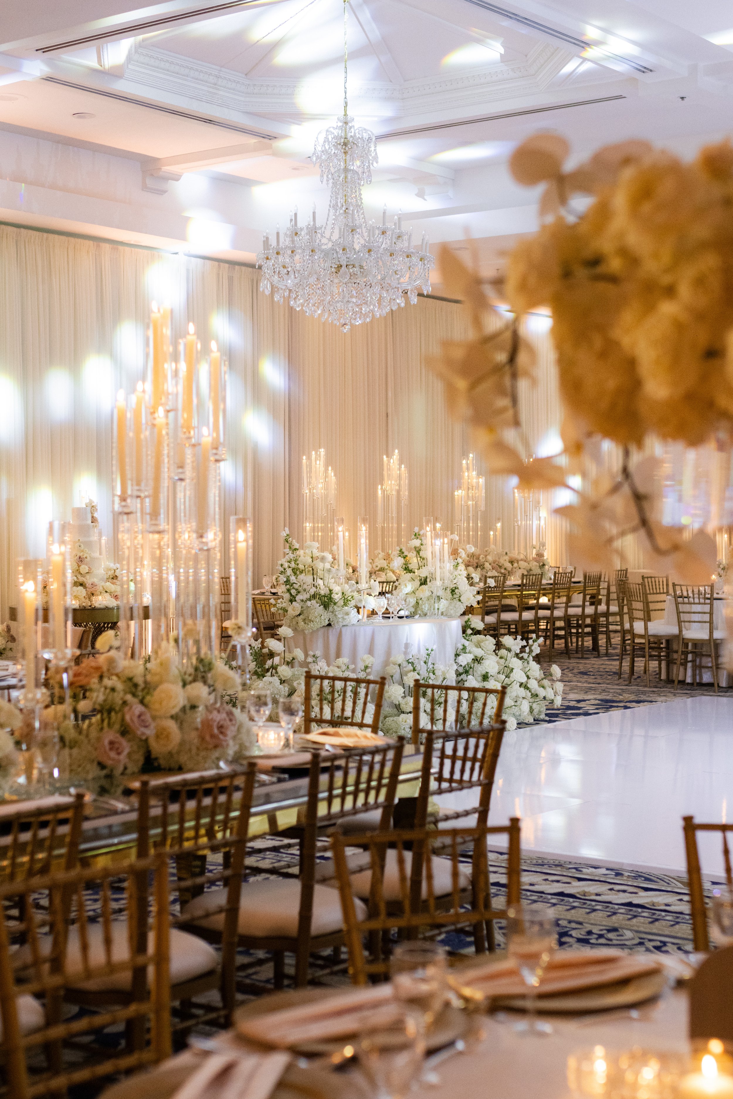 Elegant wedding reception with chandeliers, floral arrangements, candelabras, and gold chairs.